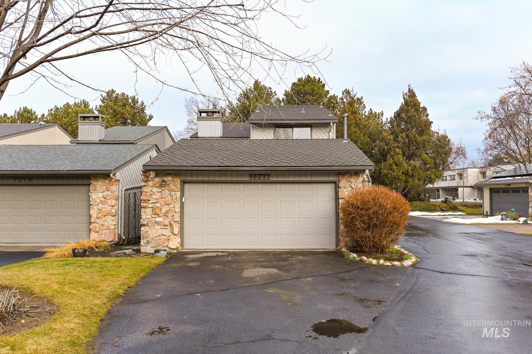 View of front of house with stone siding, a chimney, a shingled roof, and asphalt driveway