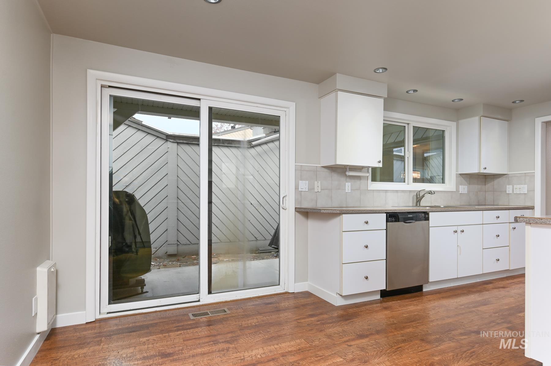 Kitchen featuring white cabinetry, stainless steel dishwasher, dark wood-style flooring, recessed lighting, and tasteful backsplash