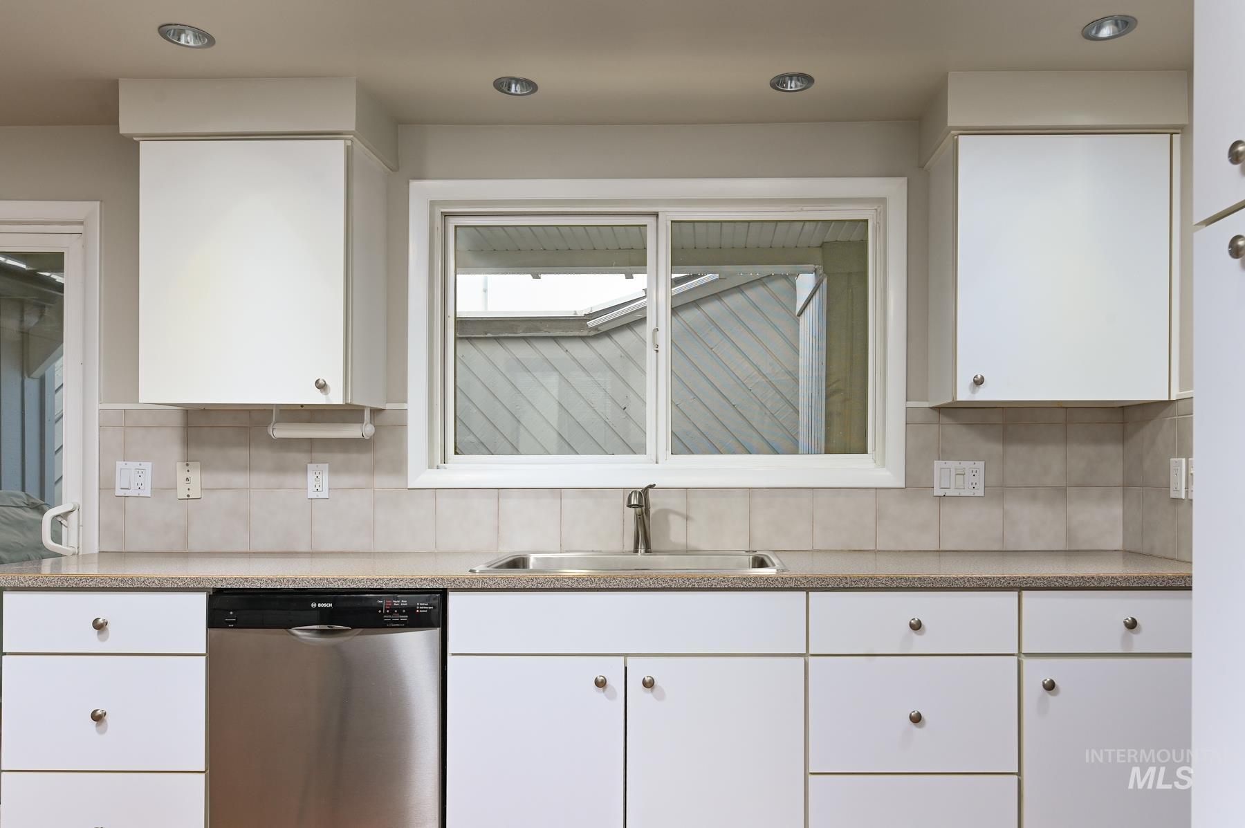 Kitchen with white cabinets, dishwasher, decorative backsplash, recessed lighting, and light stone counters