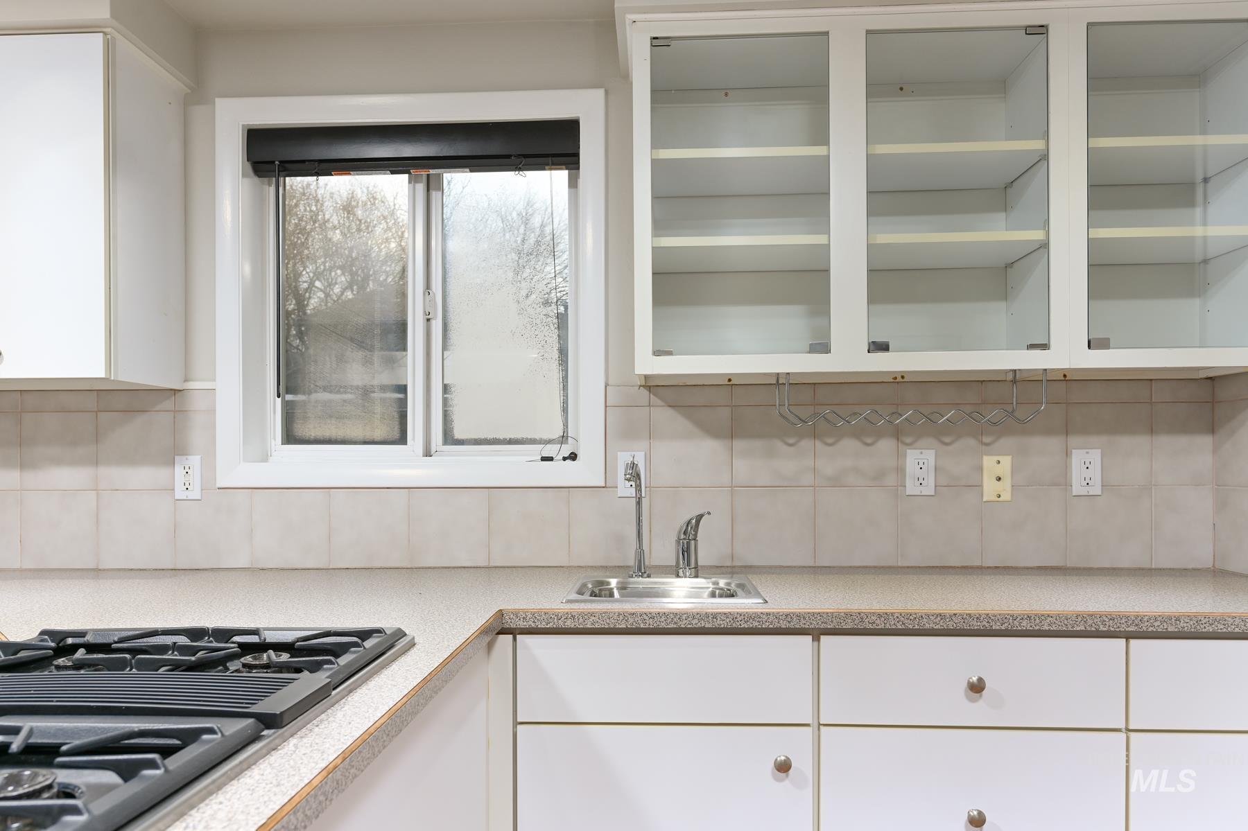 Kitchen featuring white cabinetry, stainless steel gas stovetop, light countertops, and tasteful backsplash