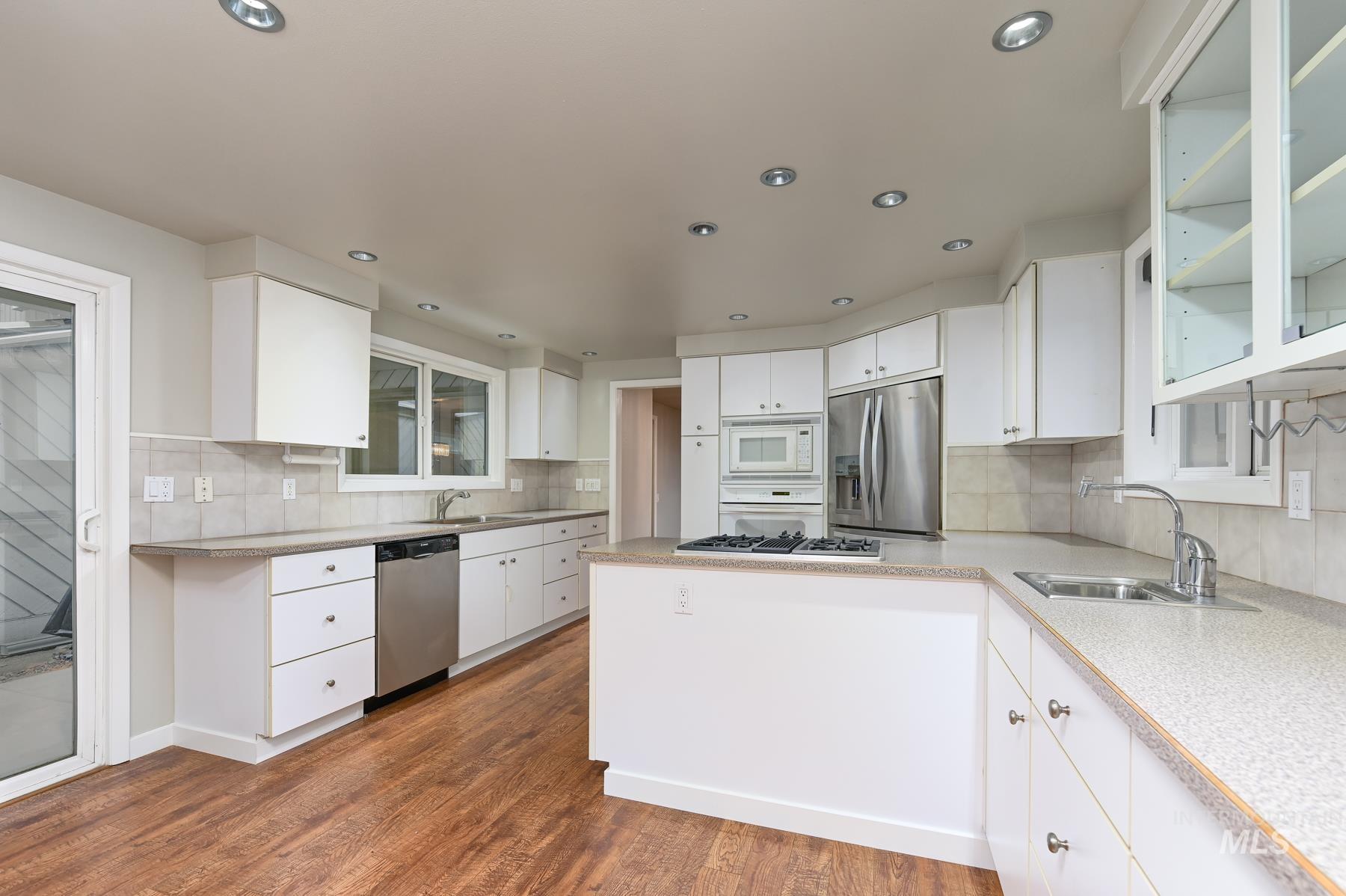 Kitchen featuring white cabinets, stainless steel appliances, dark wood-style floors, a peninsula, and backsplash