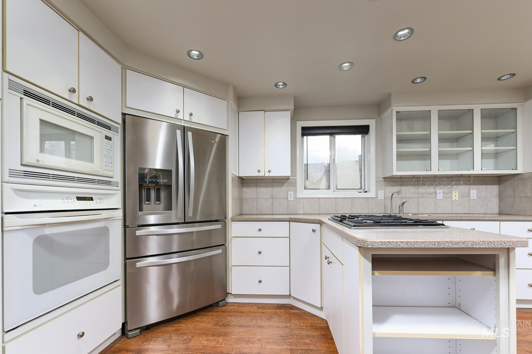 Kitchen with open shelves, white appliances, glass fronted cabinets, white cabinetry, and recessed lighting