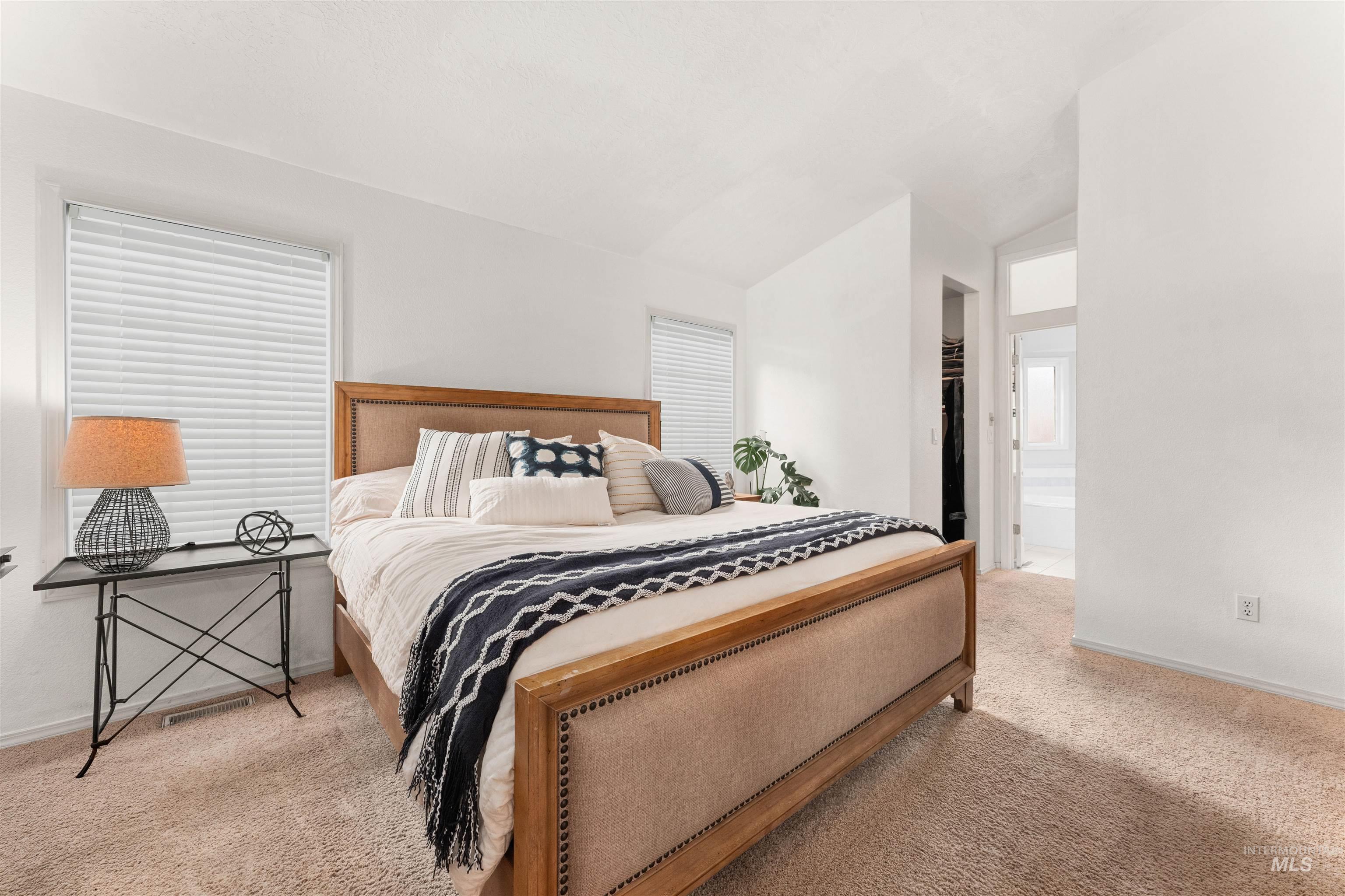 Bedroom featuring light colored carpet, vaulted ceiling, ensuite bathroom, and two walk in closets