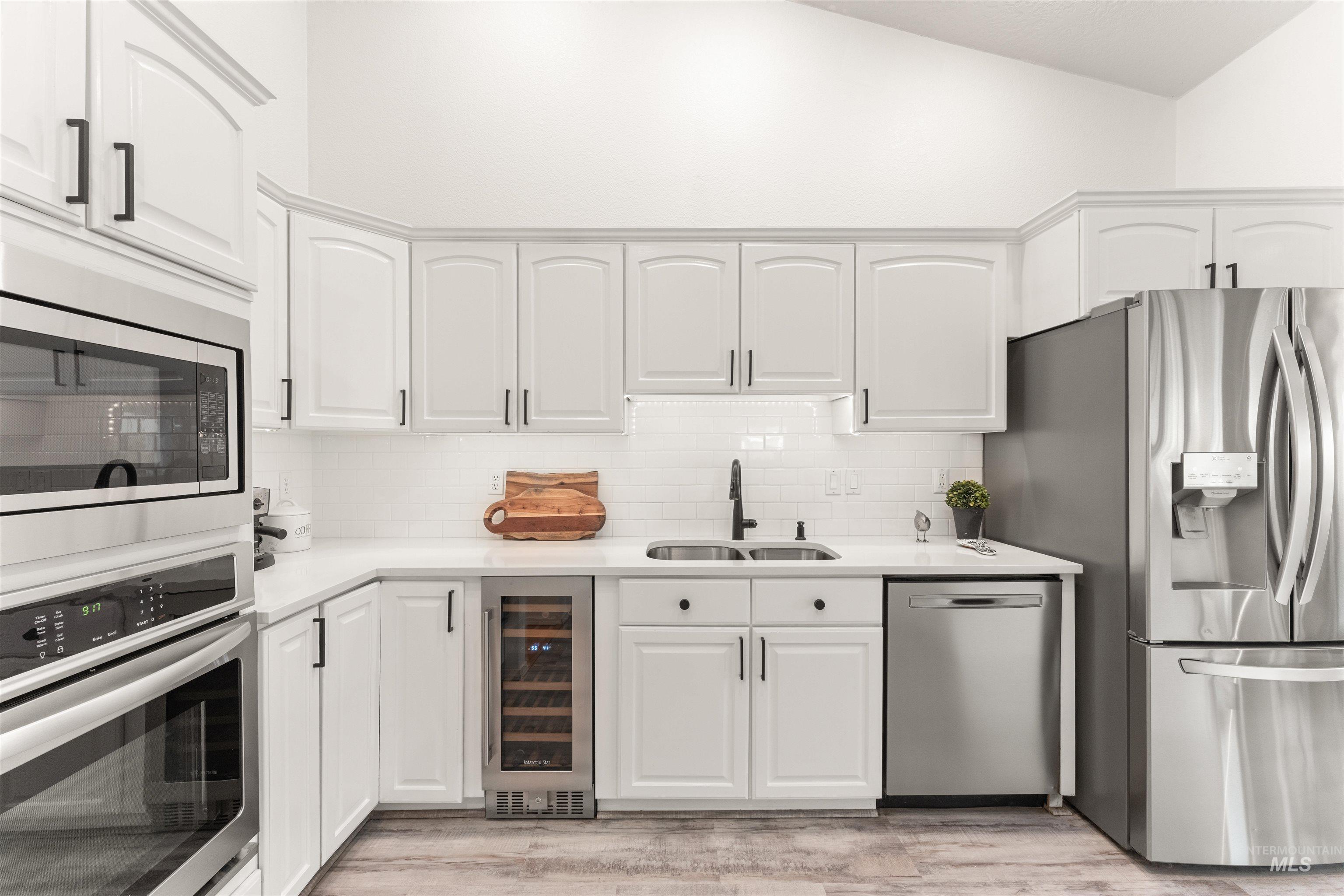 Kitchen featuring stainless steel appliances, beverage cooler, decorative backsplash, white cabinets, and vaulted ceiling