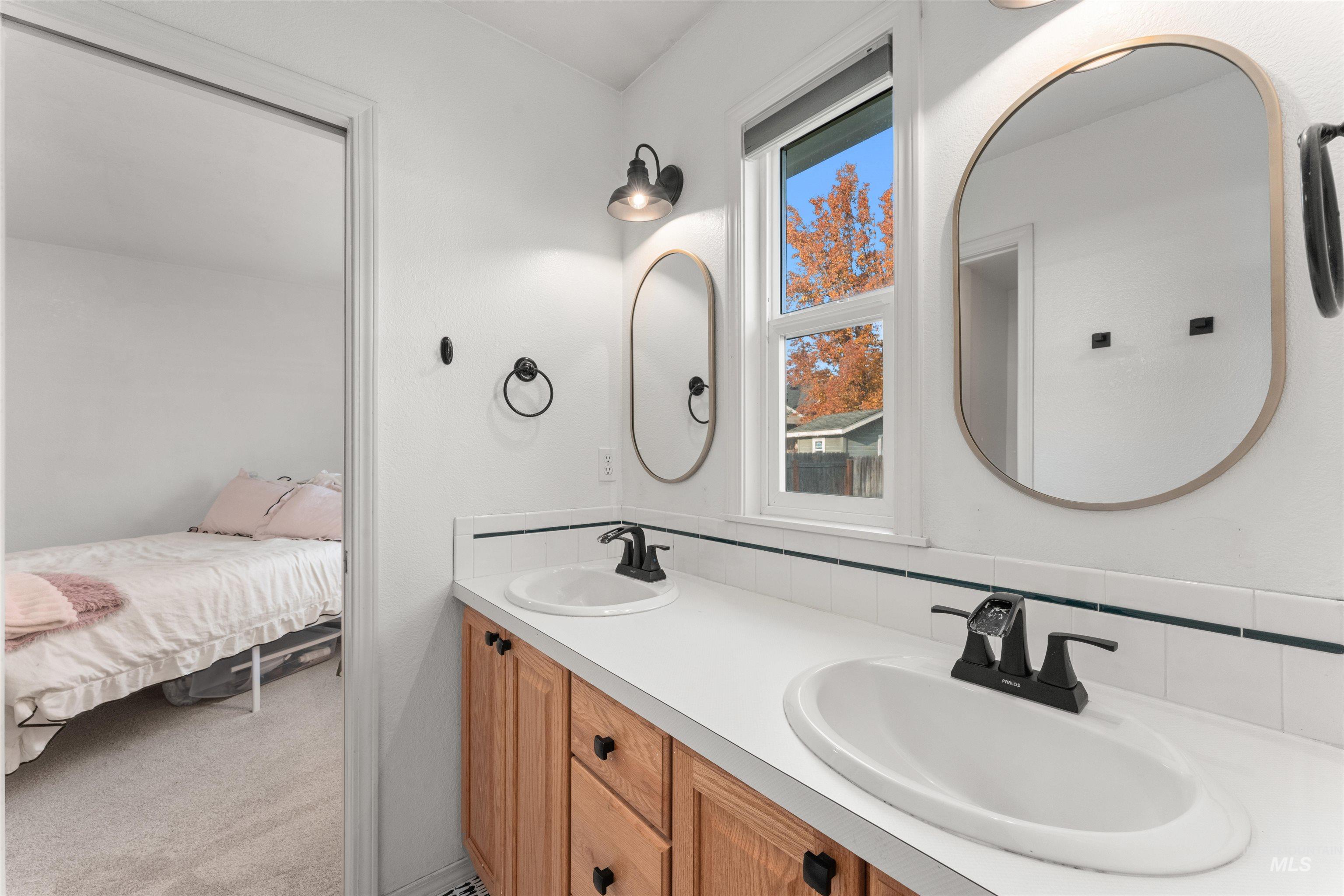 Jack and Jill bathroom with double vanity, light carpet, and decorative backsplash