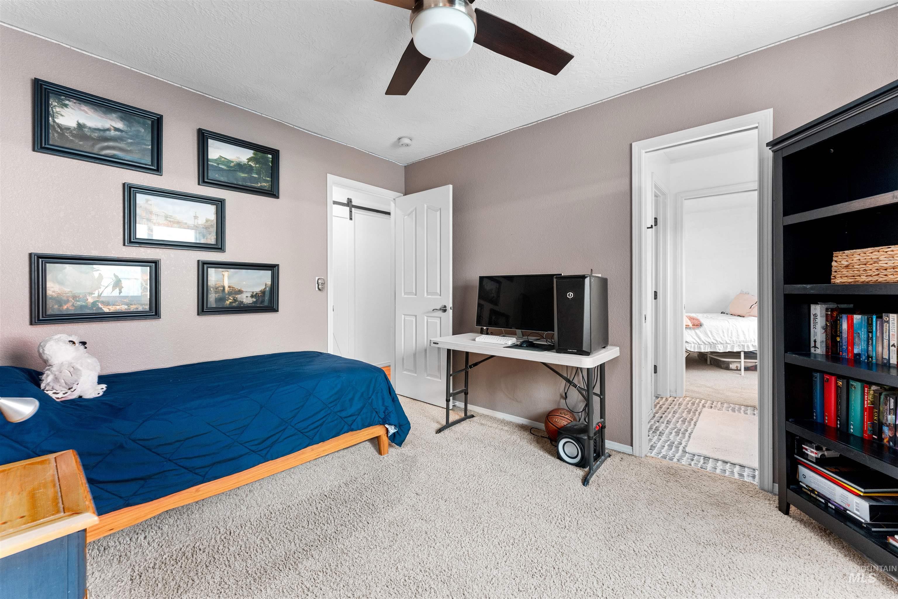 Carpeted bedroom featuring a barn door, a ceiling fan, and a textured ceiling