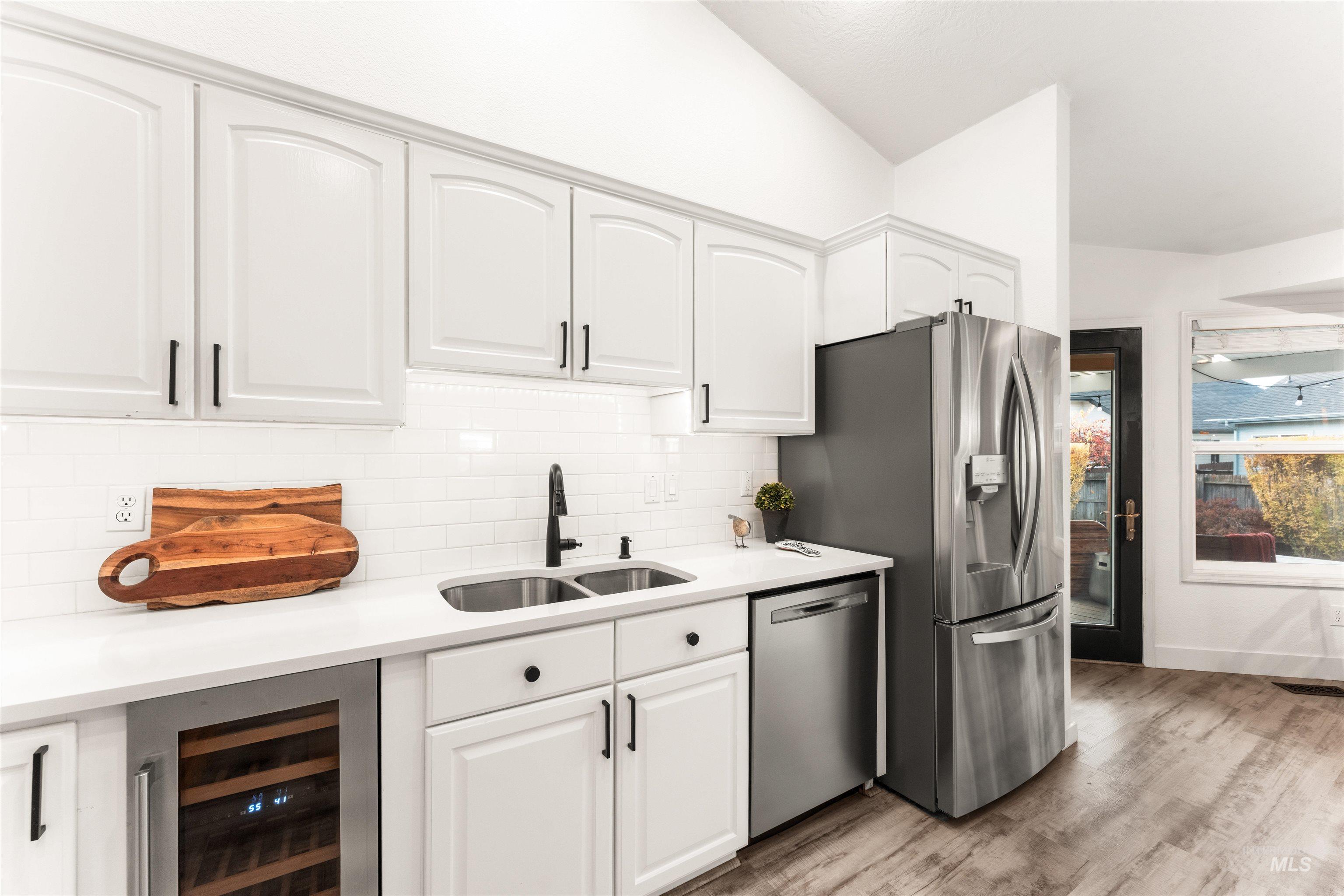 Kitchen featuring backsplash, wine cooler, light wood finished floors, appliances with stainless steel finishes, and white cabinetry