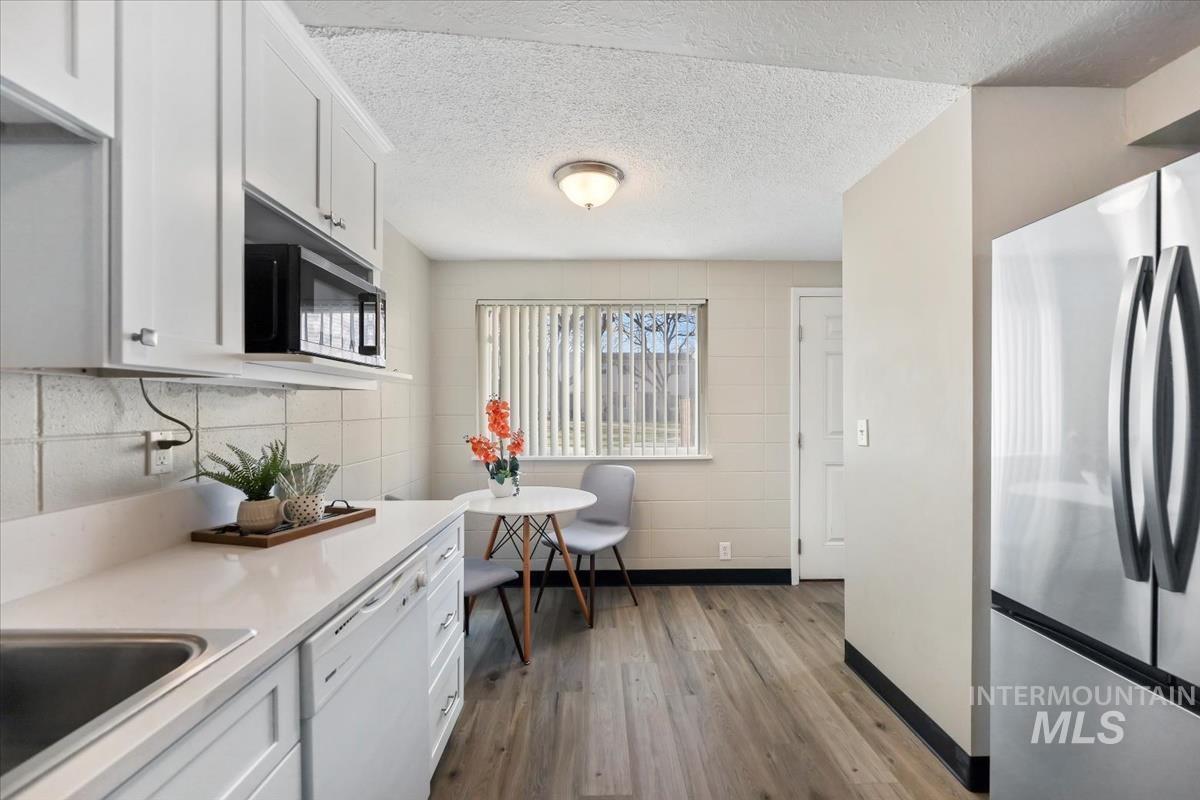 Kitchen with freestanding refrigerator, white cabinets, dishwasher, light wood finished floors, and a textured ceiling