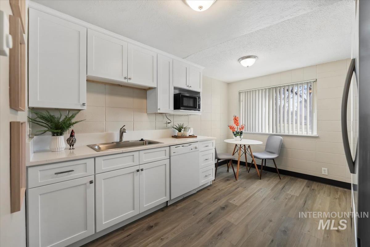 Kitchen with white cabinets, light countertops, freestanding refrigerator, a textured ceiling, and white dishwasher