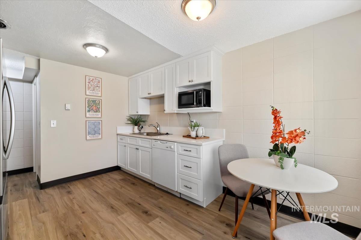 Kitchen with light countertops, light wood-type flooring, white cabinetry, a textured ceiling, and dishwasher