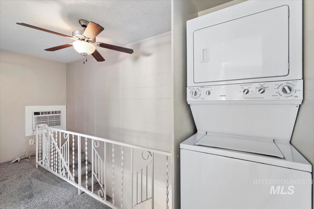 Laundry area with stacked washing machine and dryer, carpet floors, a textured ceiling, ceiling fan, and a wall mounted AC