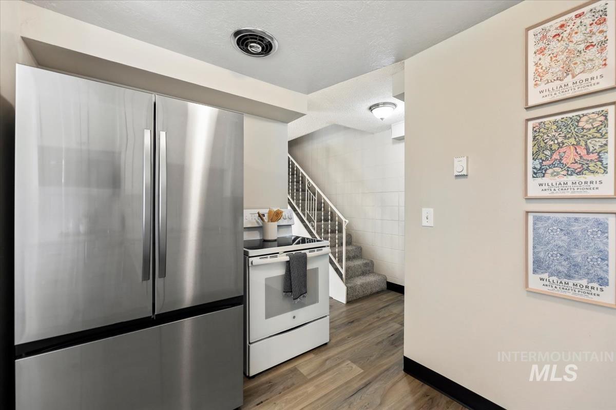 Kitchen with freestanding refrigerator, white electric stove, dark wood-type flooring, and a textured ceiling