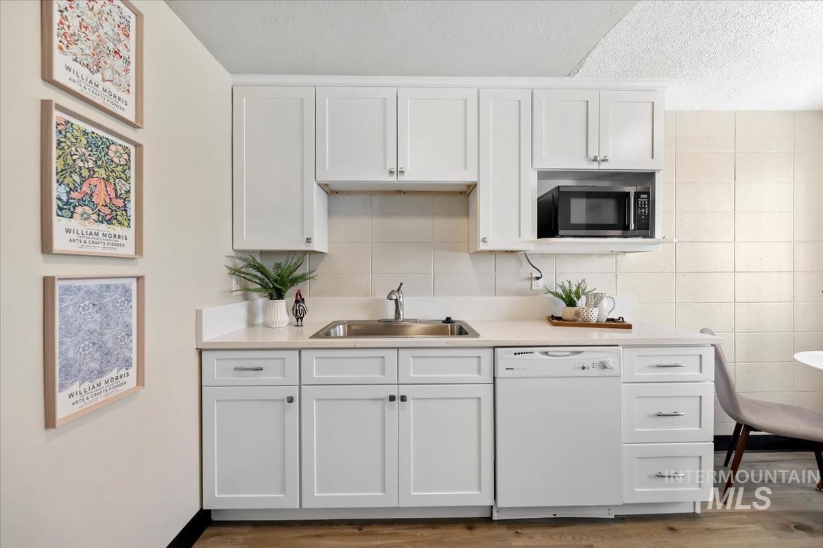 Kitchen with light countertops, dishwasher, white cabinets, a textured ceiling, and light wood-style flooring