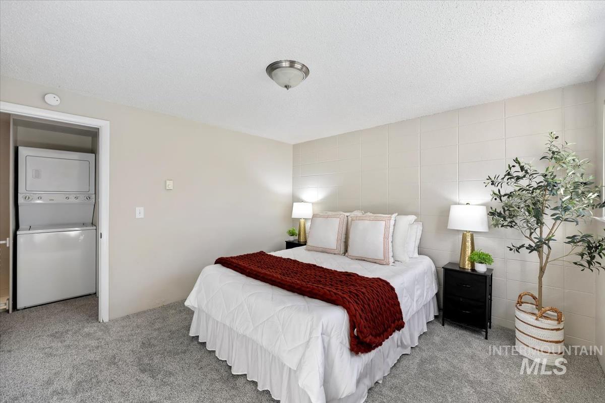 Bedroom featuring stacked washing machine and dryer, a textured ceiling, carpet flooring, and tile walls