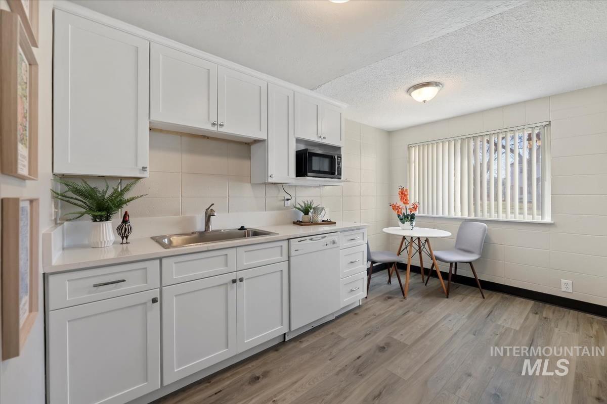 Kitchen featuring white cabinets, a textured ceiling, dishwasher, and light wood-style floors