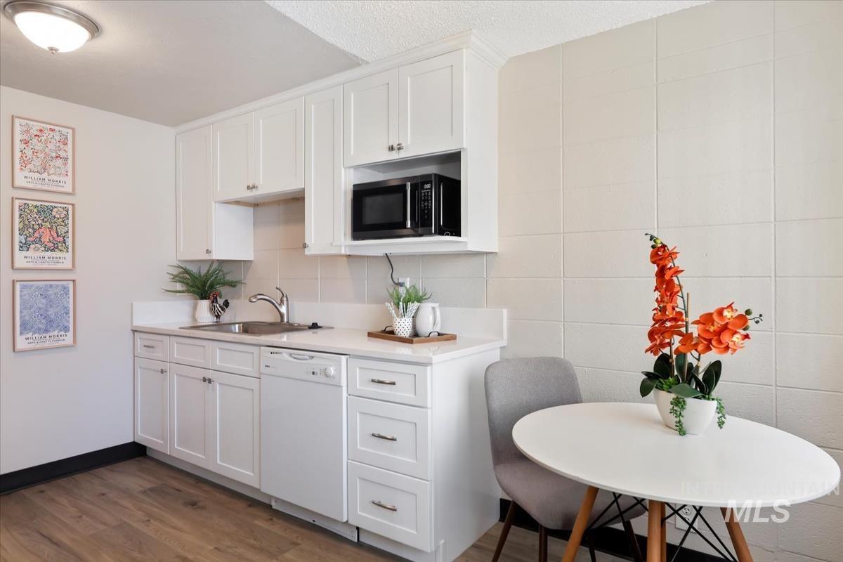 Kitchen featuring white cabinets, dark wood-type flooring, dishwasher, black microwave, and decorative backsplash