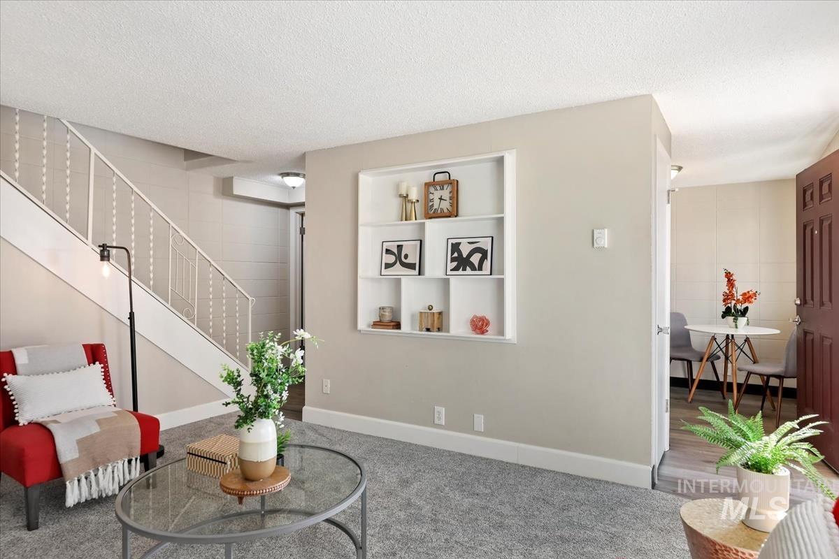 Living area with a textured ceiling, carpet, stairway, and built in shelves