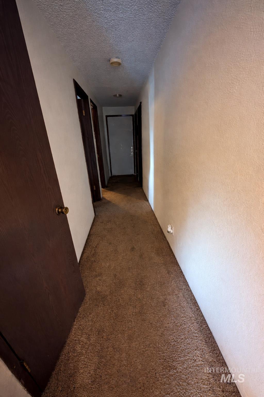 Corridor with carpet flooring, a textured ceiling, and a textured wall