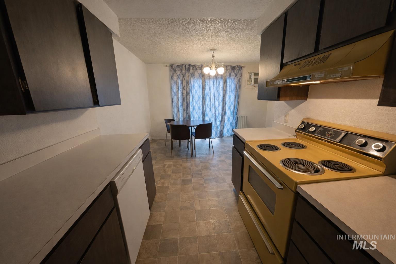Kitchen featuring electric range oven, light countertops, hanging lights, dishwasher, and a textured ceiling