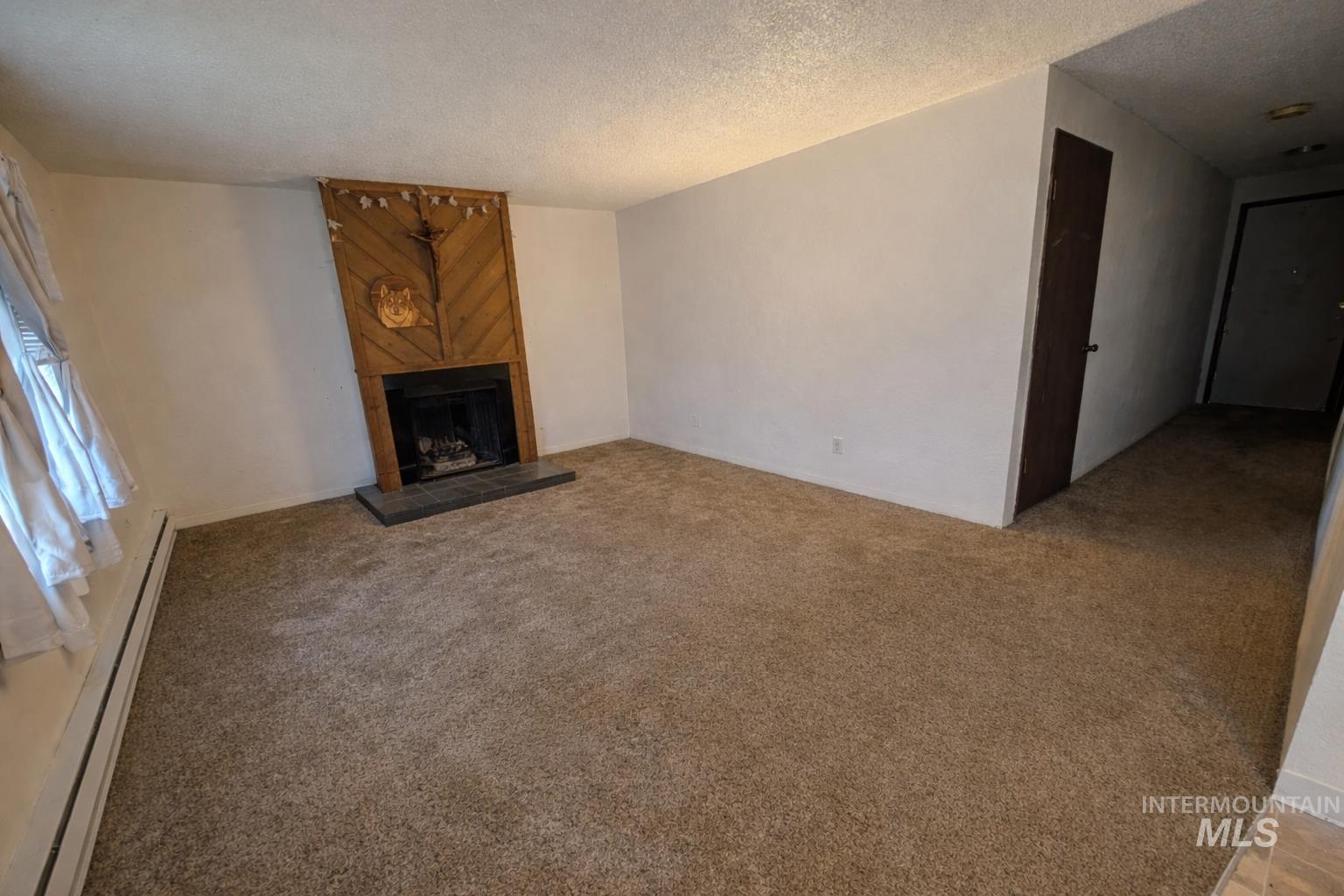 Unfurnished living room with a baseboard radiator, a fireplace, a textured ceiling, and light carpet