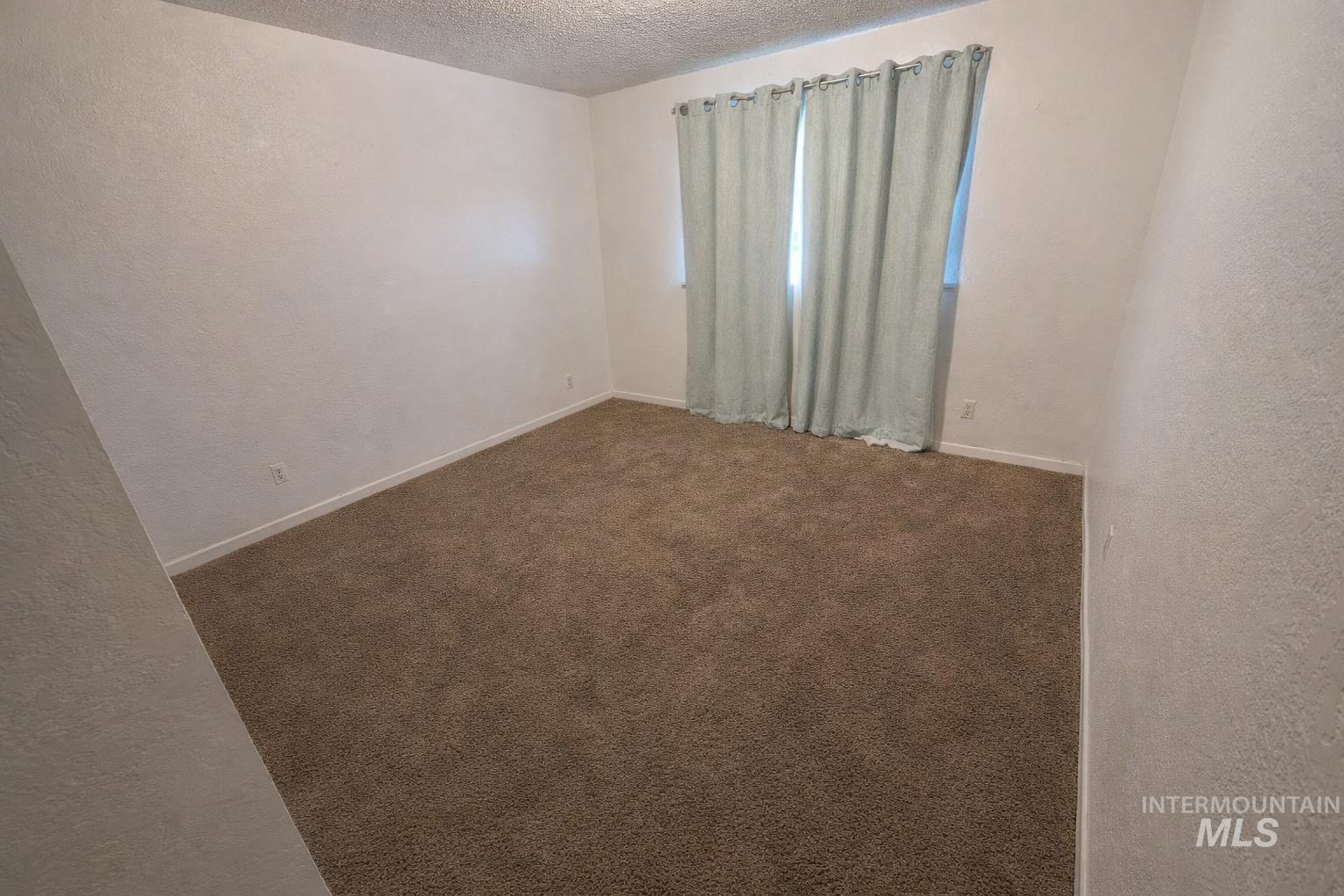 Spare room featuring a textured wall, carpet flooring, and a textured ceiling