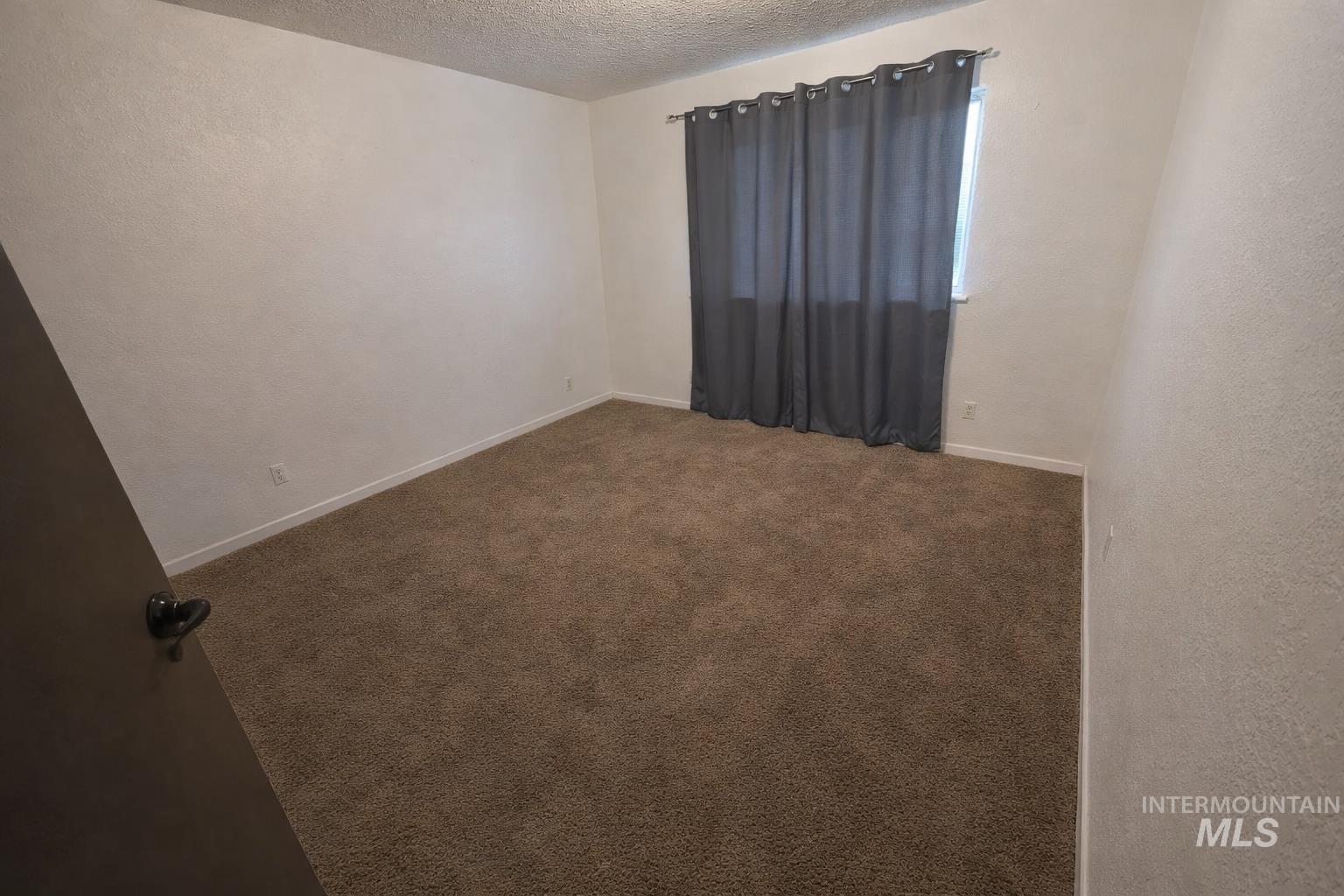 Empty room with a textured wall, dark colored carpet, and a textured ceiling