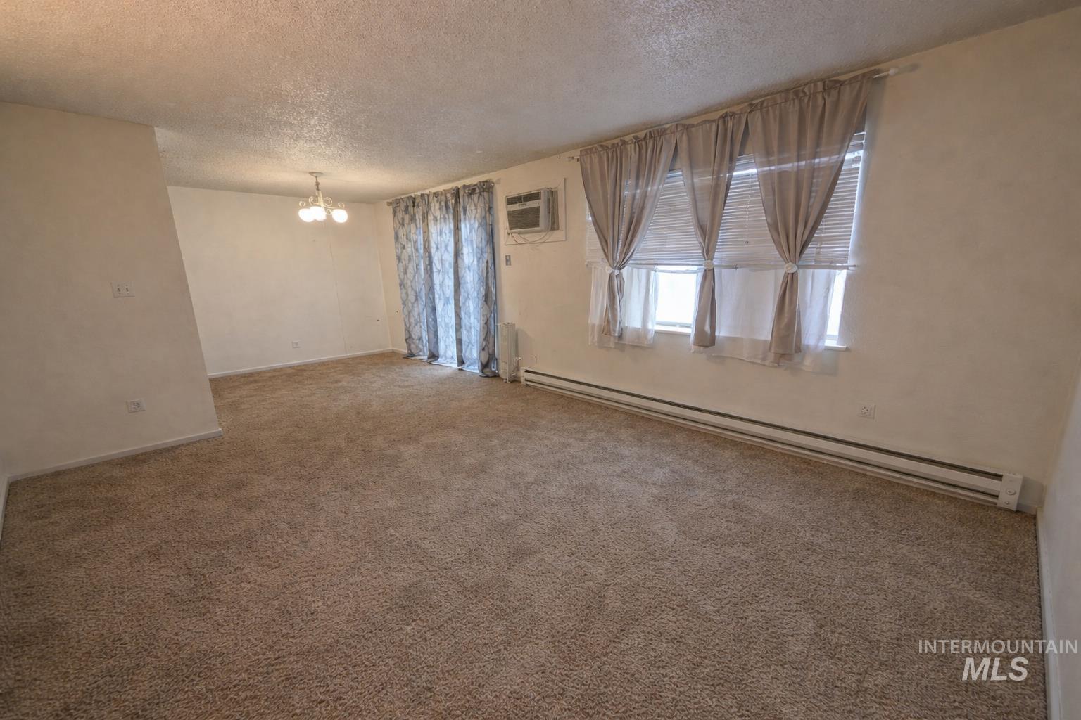 Unfurnished room featuring a baseboard heating unit, a textured ceiling, carpet, and hanging lights