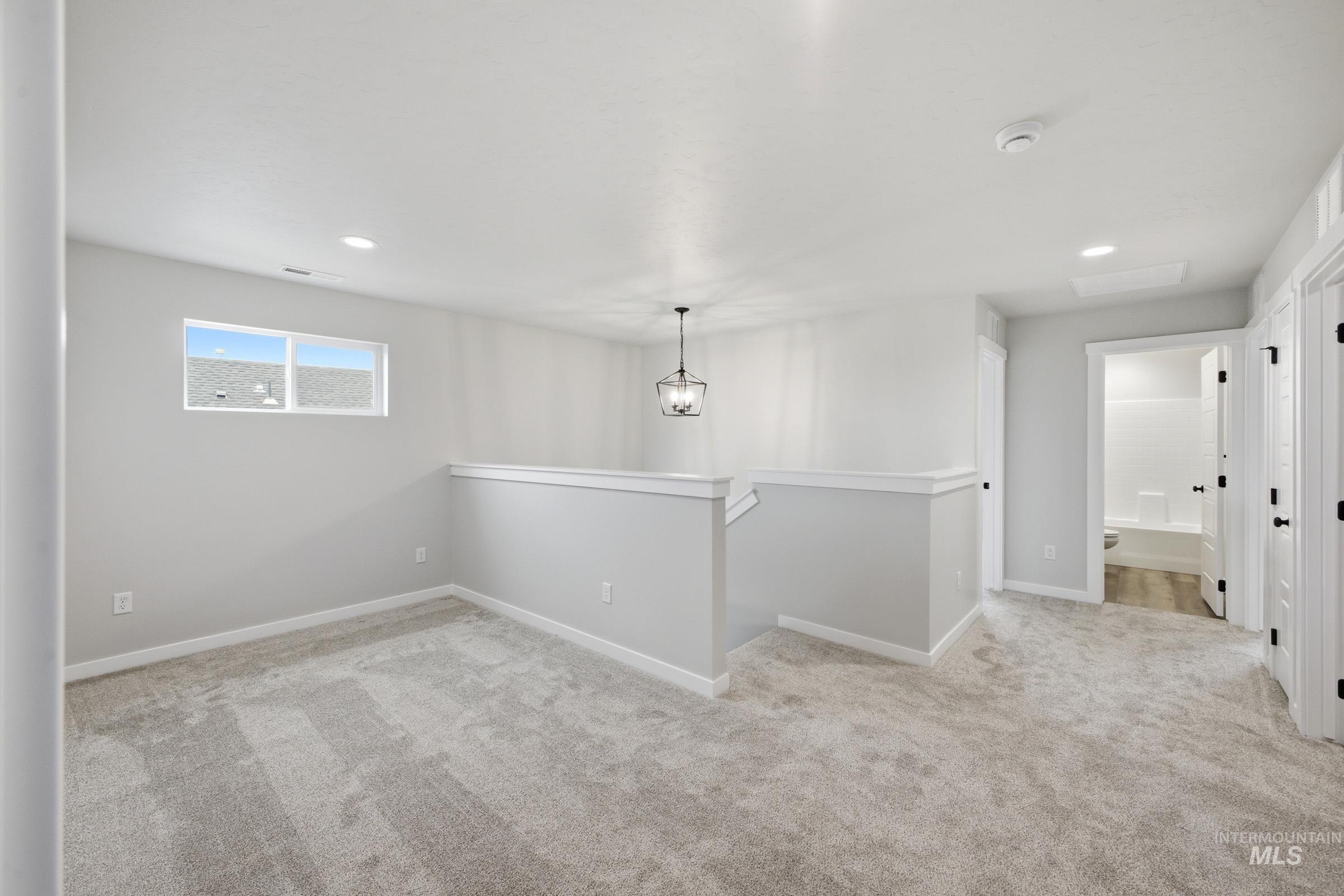 Open loft area featuring light gray carpeting, recessed lighting, and a contemporary hanging light fixture