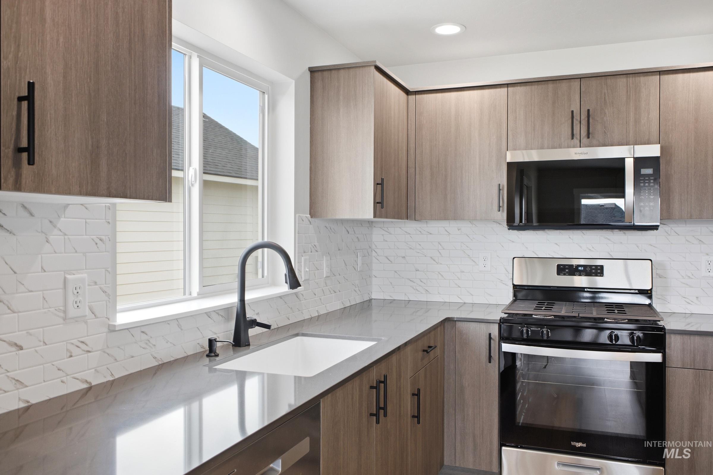 Contemporary kitchen featuring wood-grain cabinetry with matte black hardware, stone-look countertops, and a white subway tile backsplash