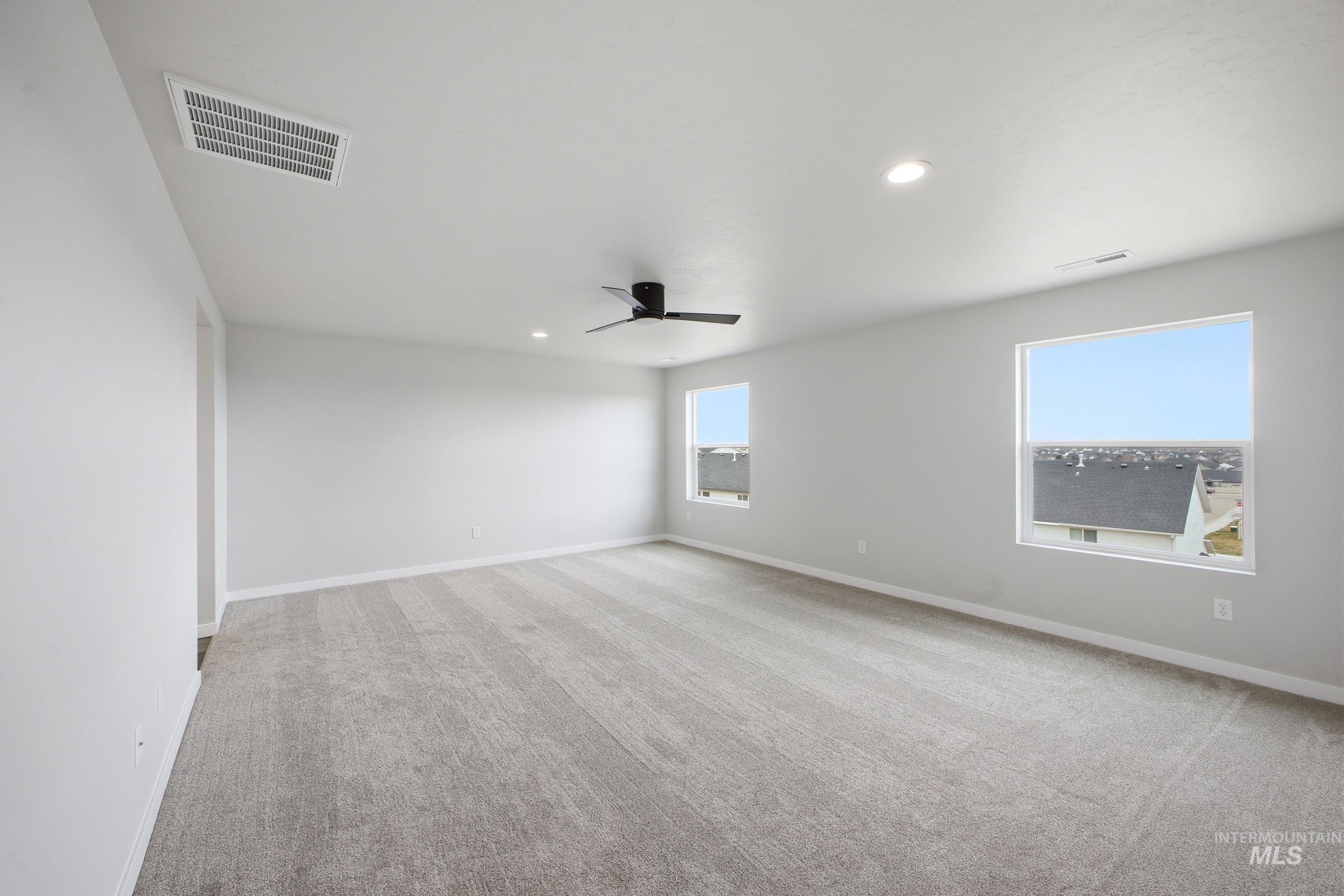 Spacious room featuring light gray carpeting, crisp white walls, multiple windows, a ceiling-mounted fan, and recessed lighting