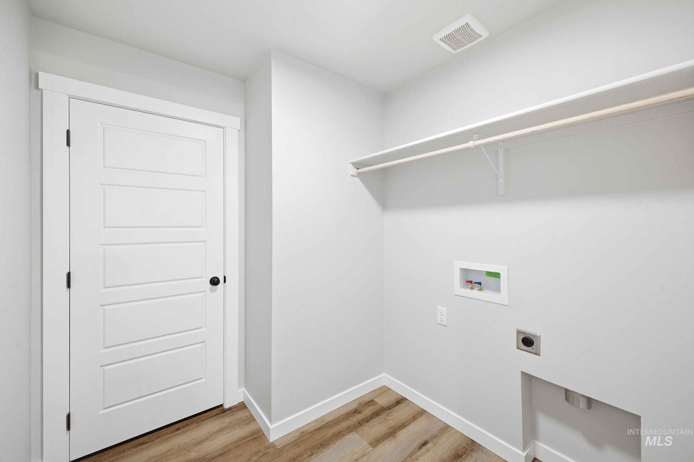 Dedicated utility area featuring wood-finish flooring, white baseboards, and light gray walls