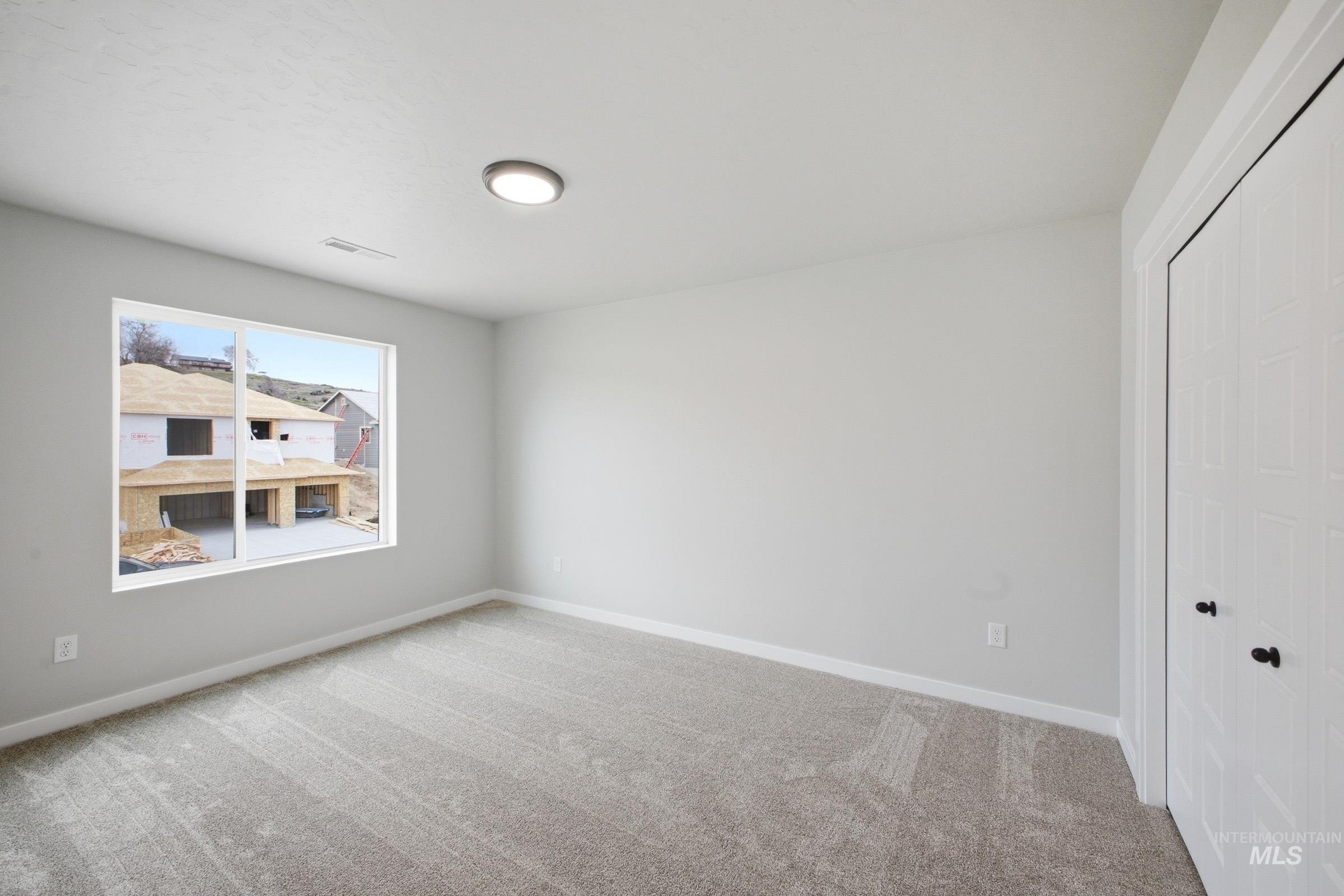 Spacious room featuring light gray carpeting, neutral-toned walls, and a large window