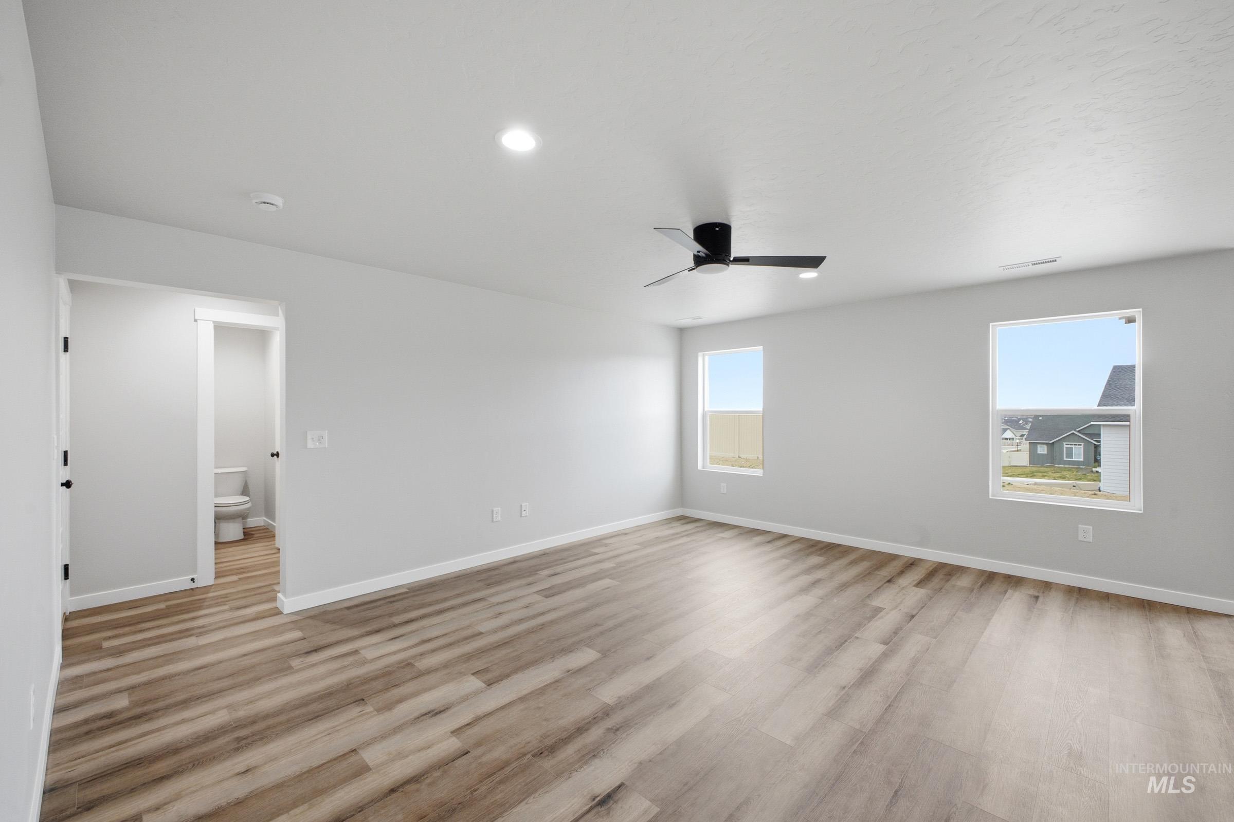 Spacious room featuring wood-finish flooring, two windows, recessed lighting, and a ceiling fan