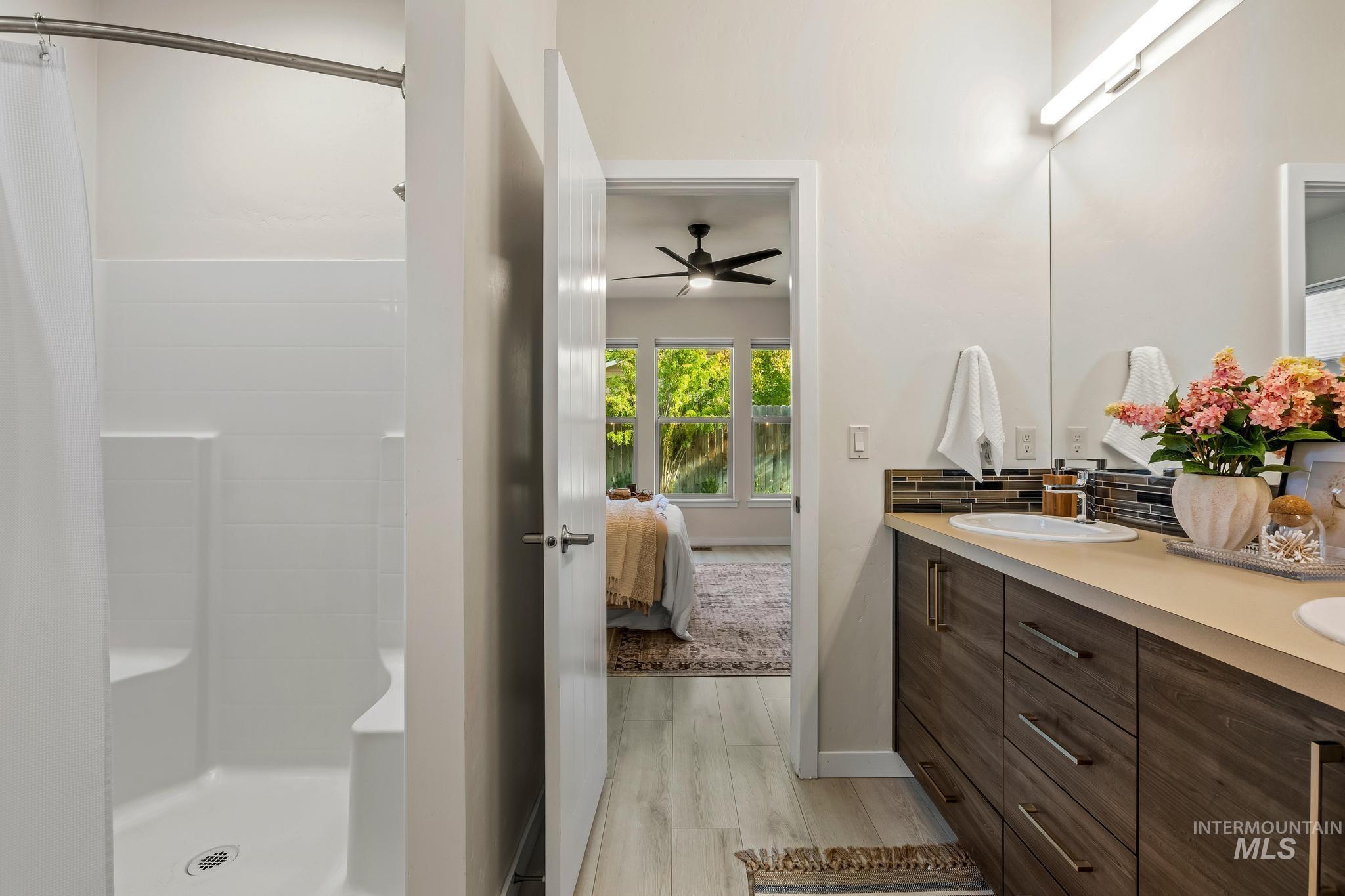 Ensuite bathroom with light wood-type flooring, double vanity, a shower with shower curtain, and a ceiling fan