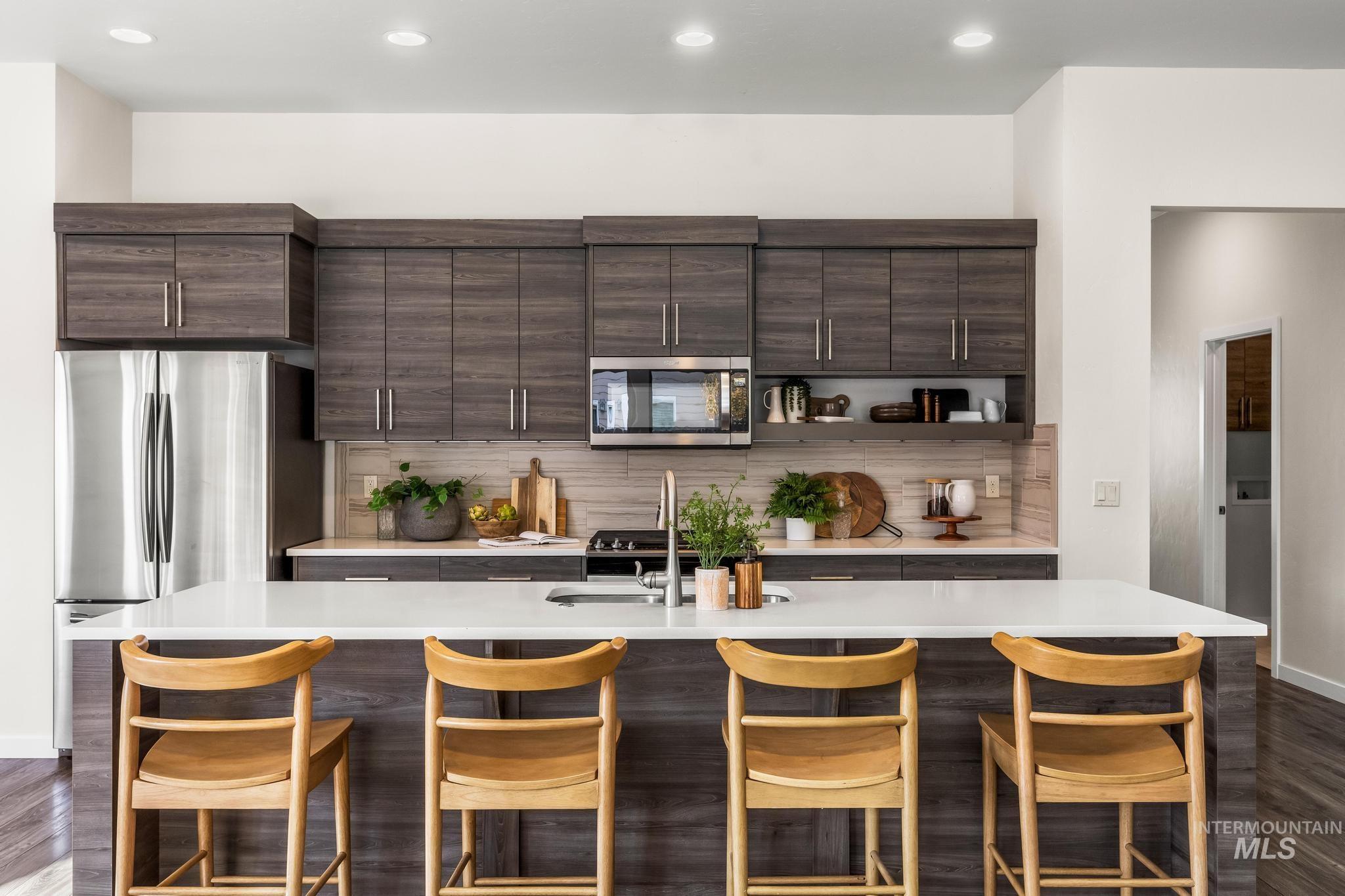 Kitchen featuring dark brown cabinets, tasteful backsplash, appliances with stainless steel finishes, an island with sink, and a breakfast bar area