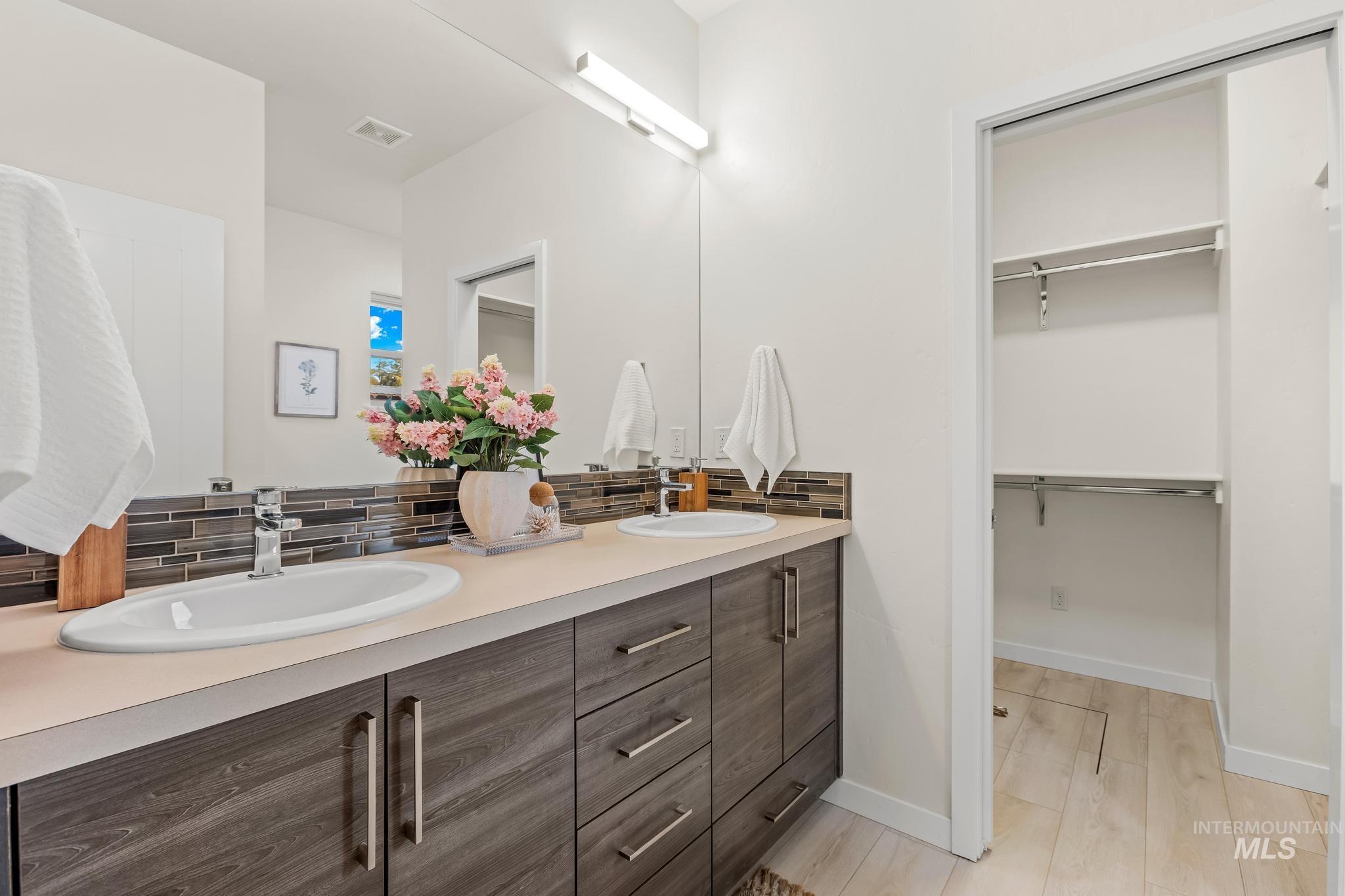 Bathroom with double vanity, backsplash, a spacious closet, and light wood-style floors