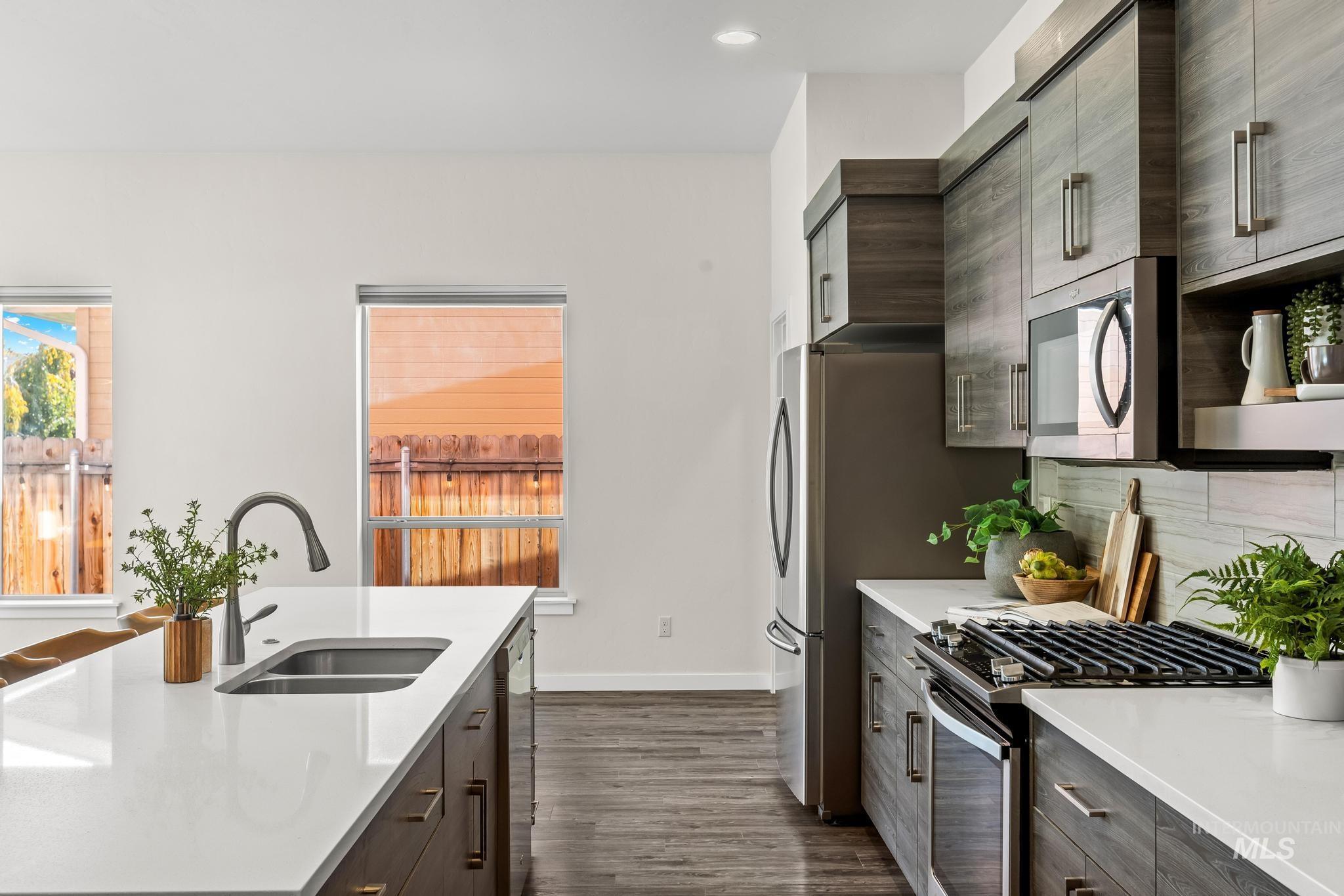 Kitchen with dark brown cabinetry, modern cabinets, appliances with stainless steel finishes, dark wood finished floors, and light stone countertops