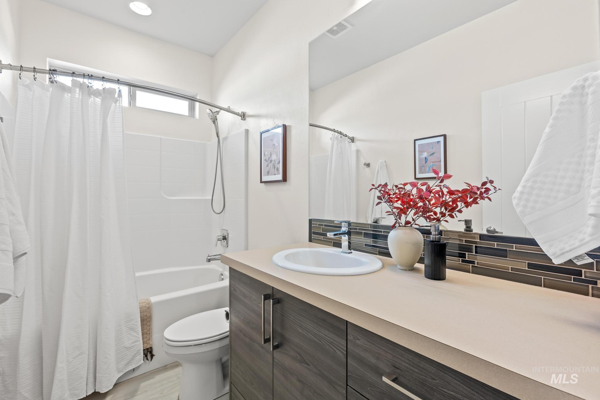 Bathroom with shower / bathtub combination with curtain, vanity, and backsplash