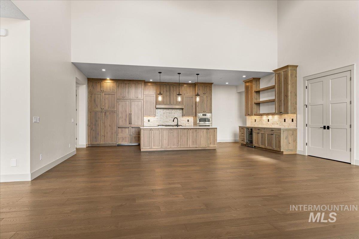 Kitchen featuring open shelves, decorative backsplash, decorative light fixtures, light countertops, and a towering ceiling