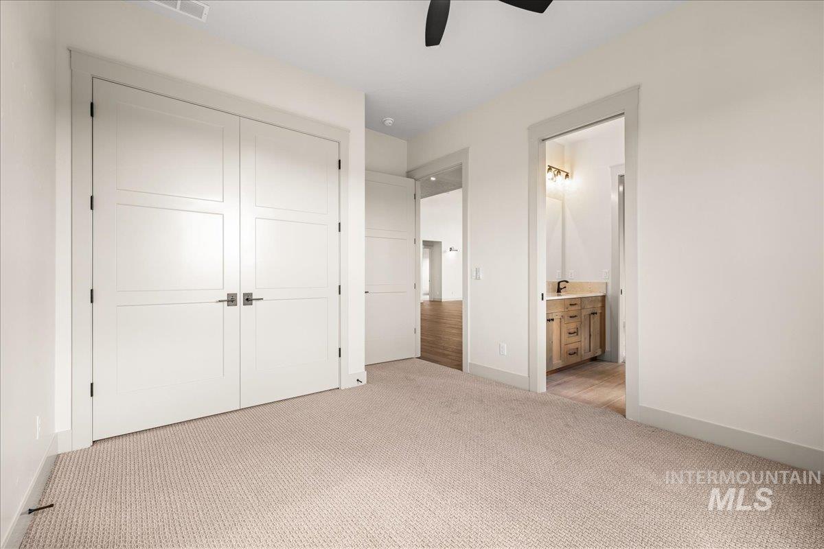 Unfurnished bedroom with light carpet, ensuite bath, a ceiling fan, and a closet