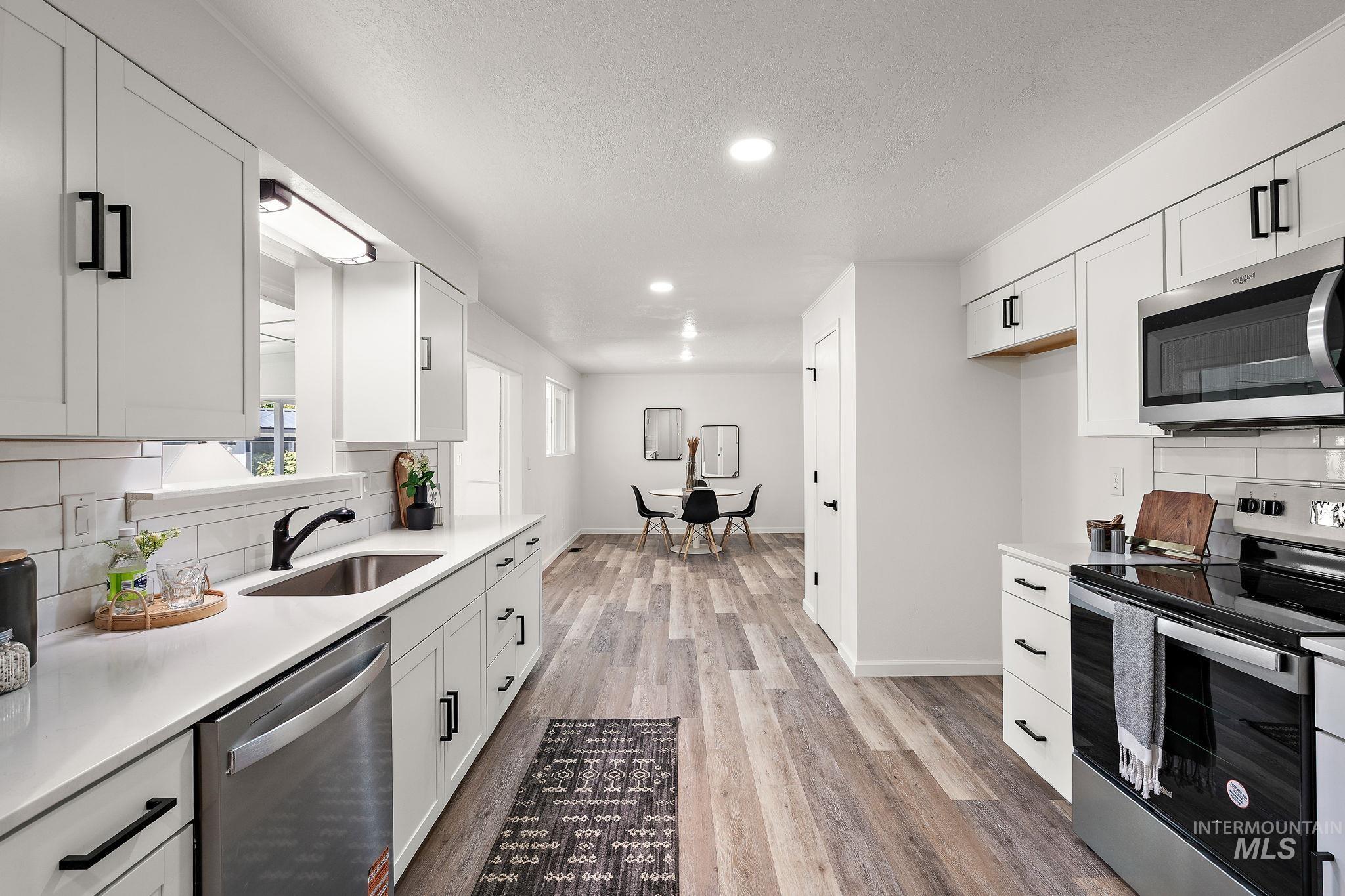 Kitchen featuring backsplash, appliances with stainless steel finishes, white cabinetry, light wood-style flooring, and recessed lighting