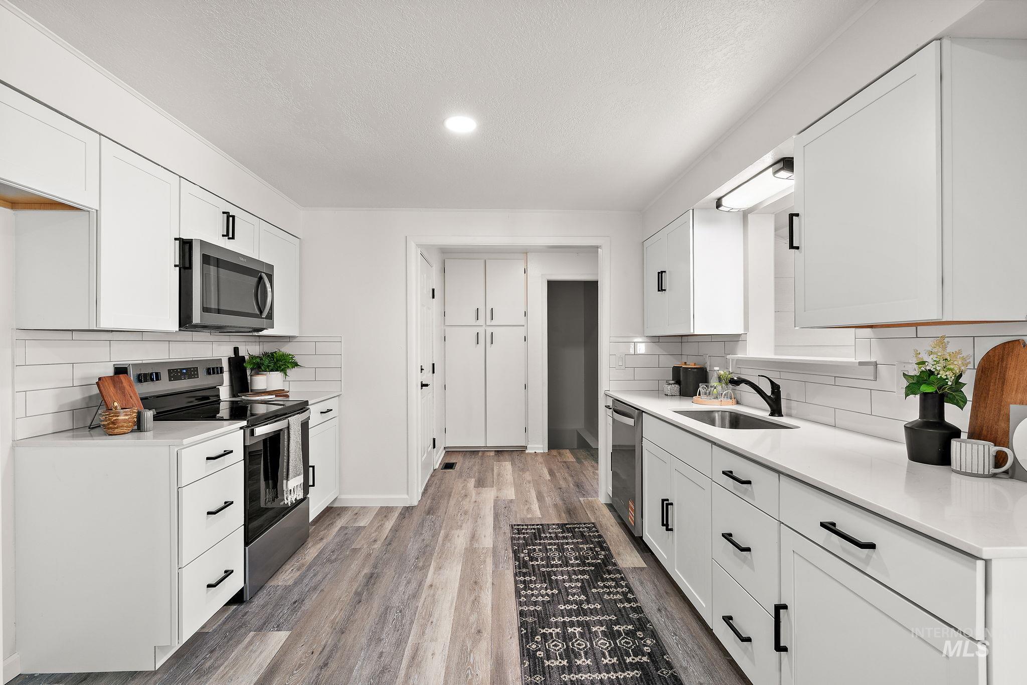 Kitchen with backsplash, stainless steel appliances, white cabinets, light wood-style flooring, and a textured ceiling