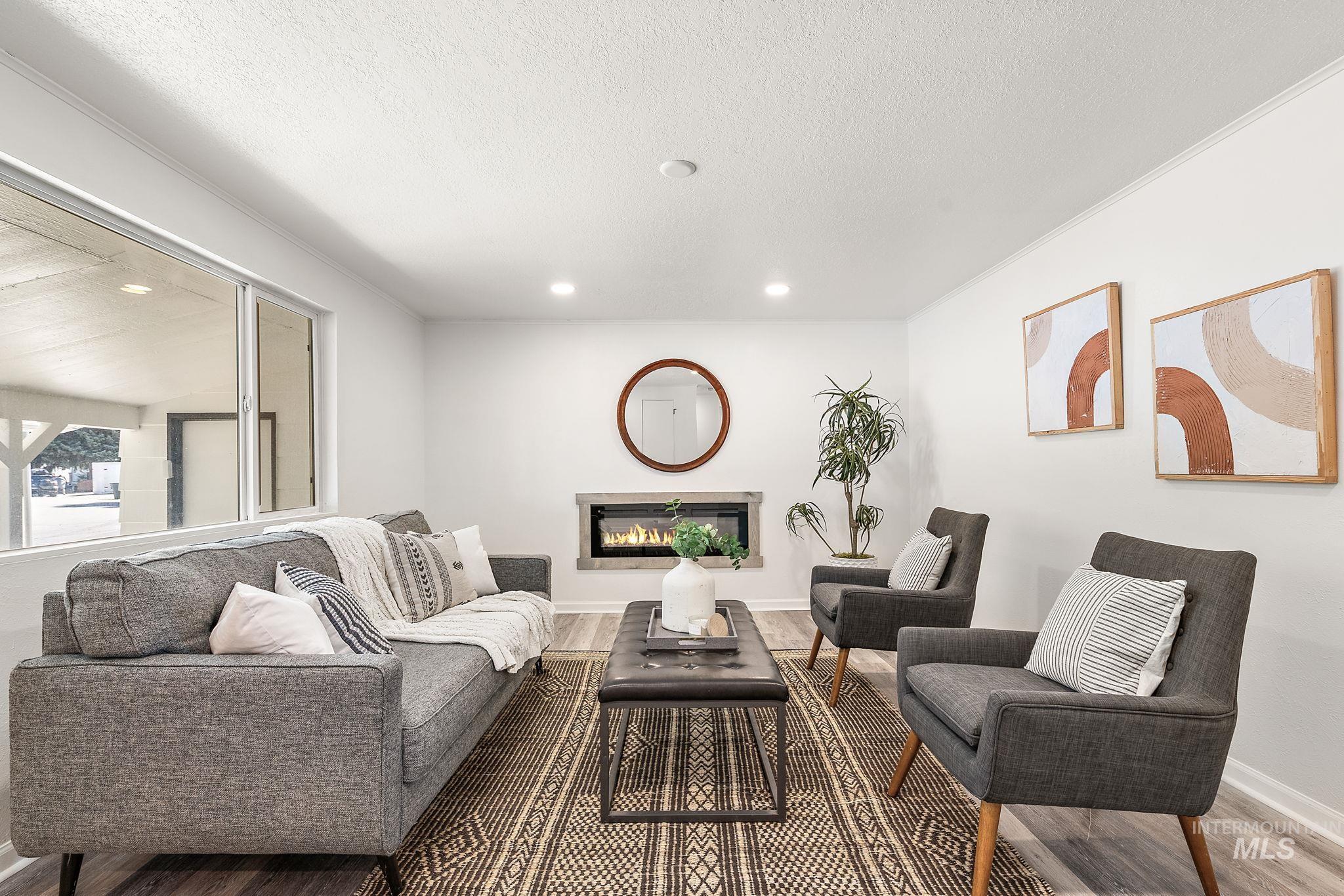 Living room with a glass covered fireplace, wood finished floors, a textured ceiling, crown molding, and recessed lighting
