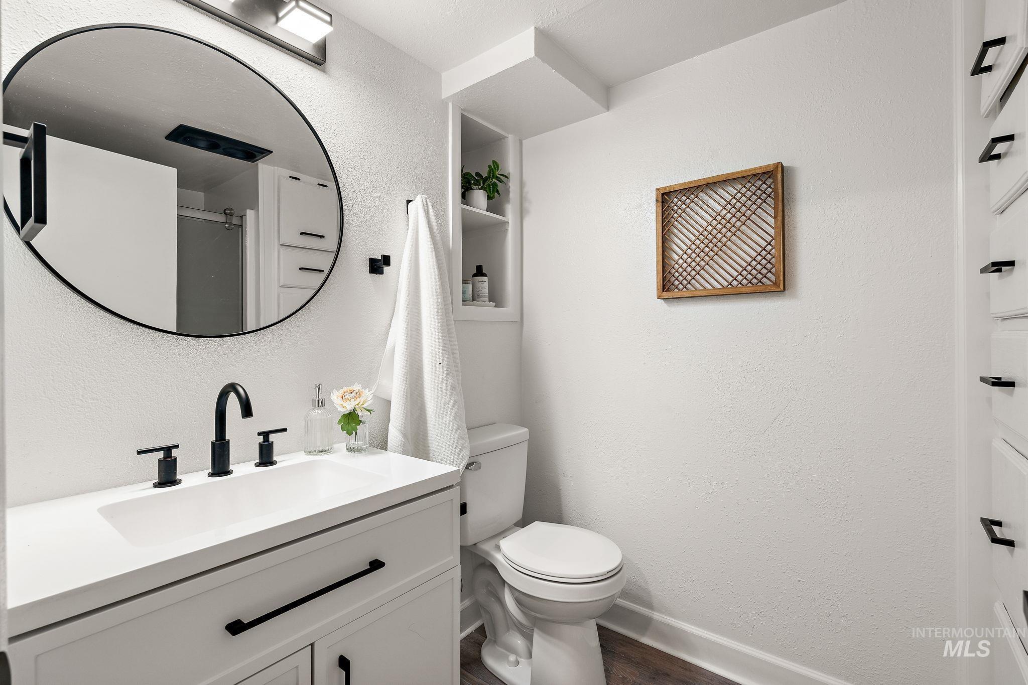 Full bathroom featuring a textured wall, vanity, dark wood-style floors, and a shower with door
