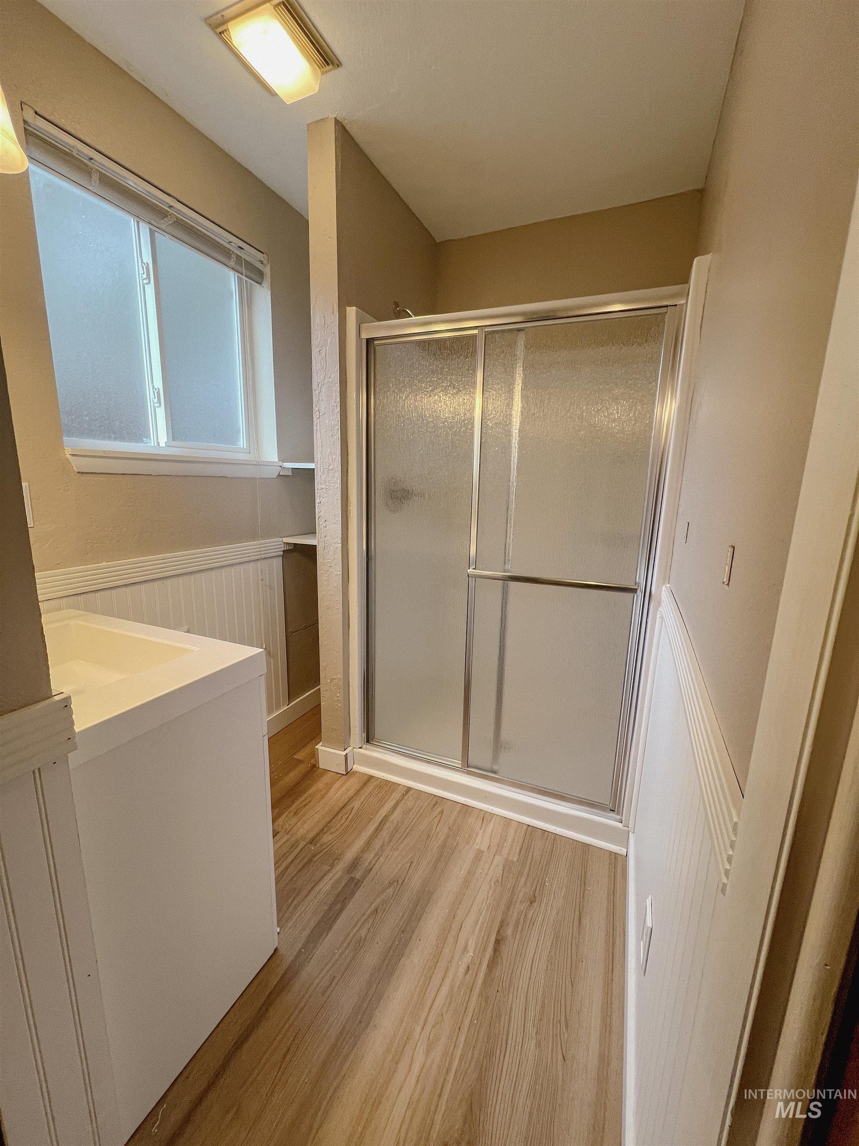 Bathroom featuring vanity, a shower stall, light wood-style flooring, and wainscoting