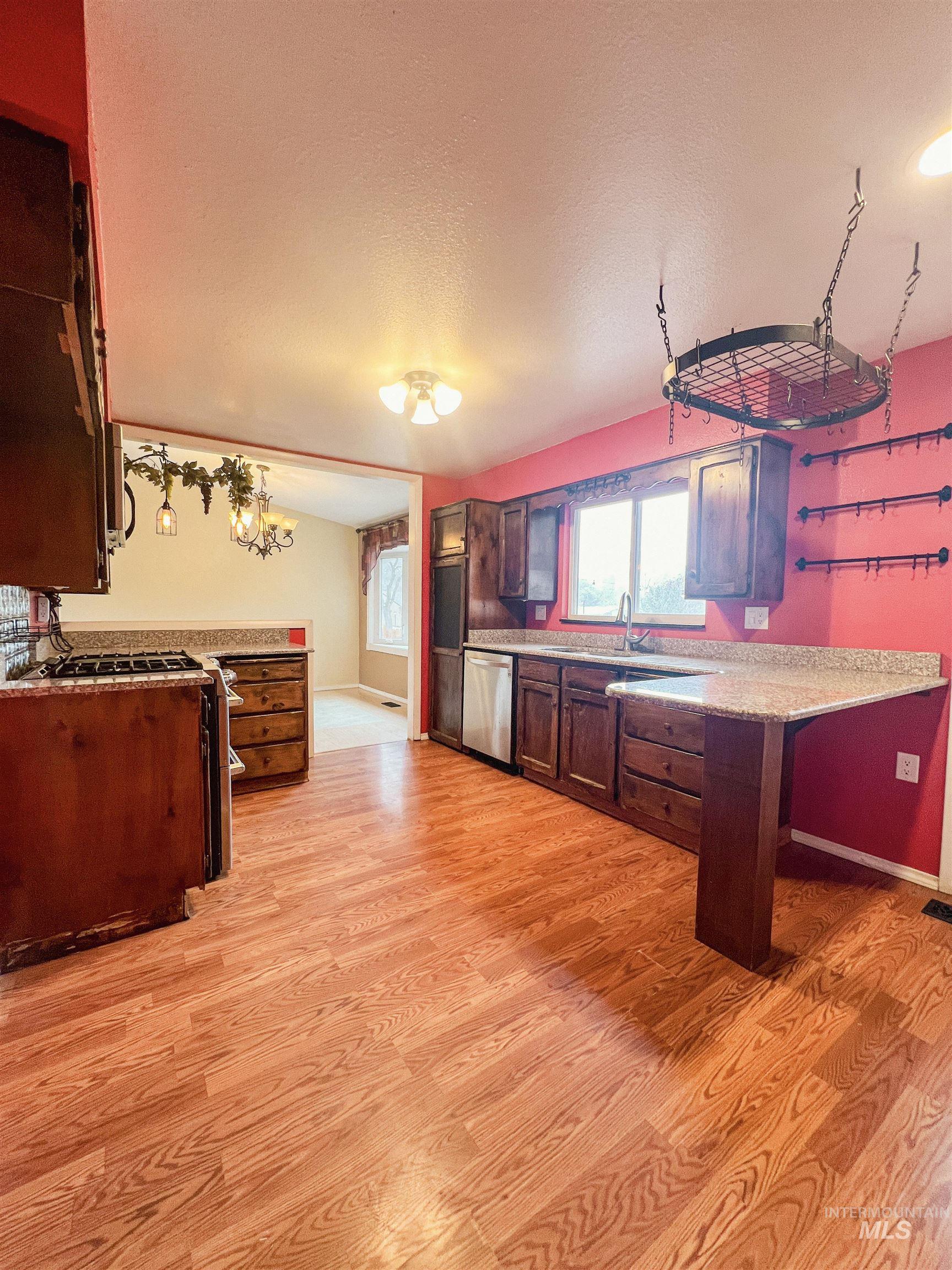 Kitchen with a peninsula, a textured ceiling, stainless steel appliances, light wood-type flooring, and light stone counters