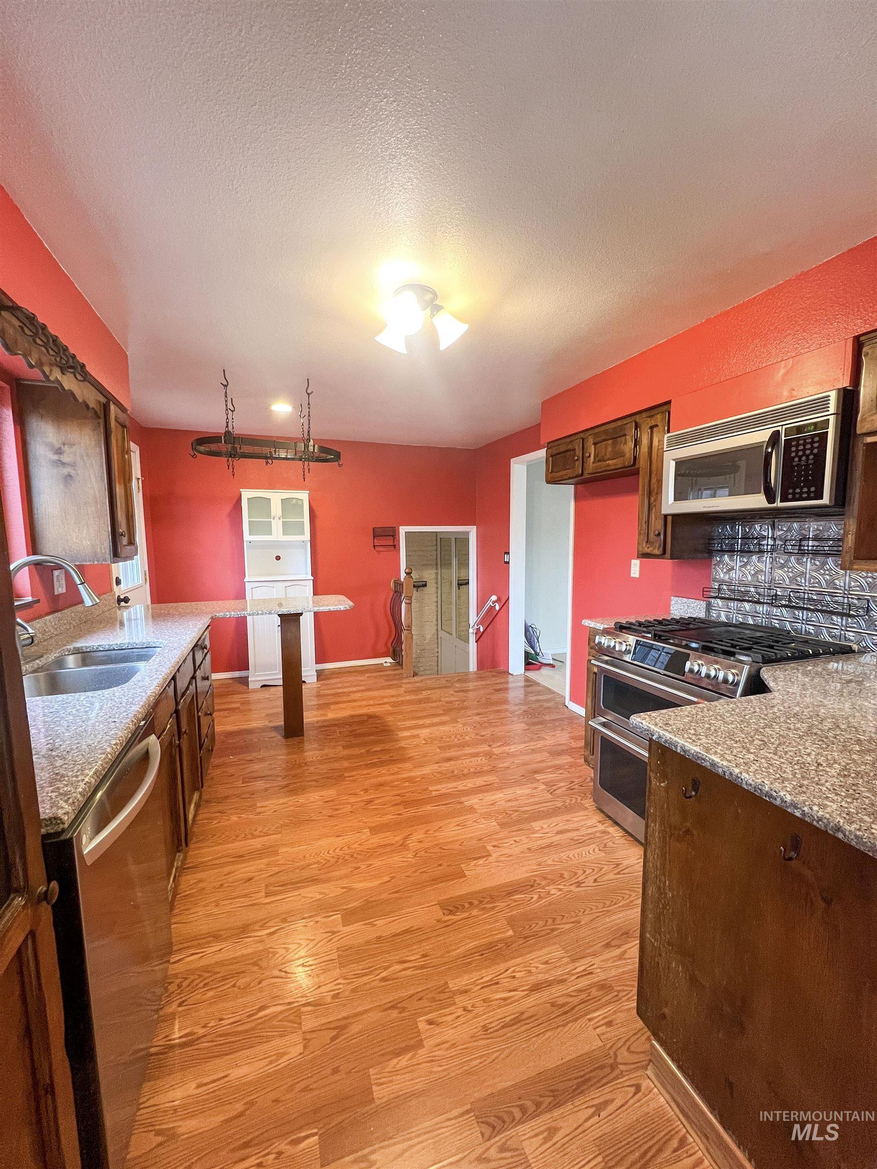 Kitchen featuring stainless steel appliances, light stone countertops, light wood-style floors, tasteful backsplash, and a textured ceiling