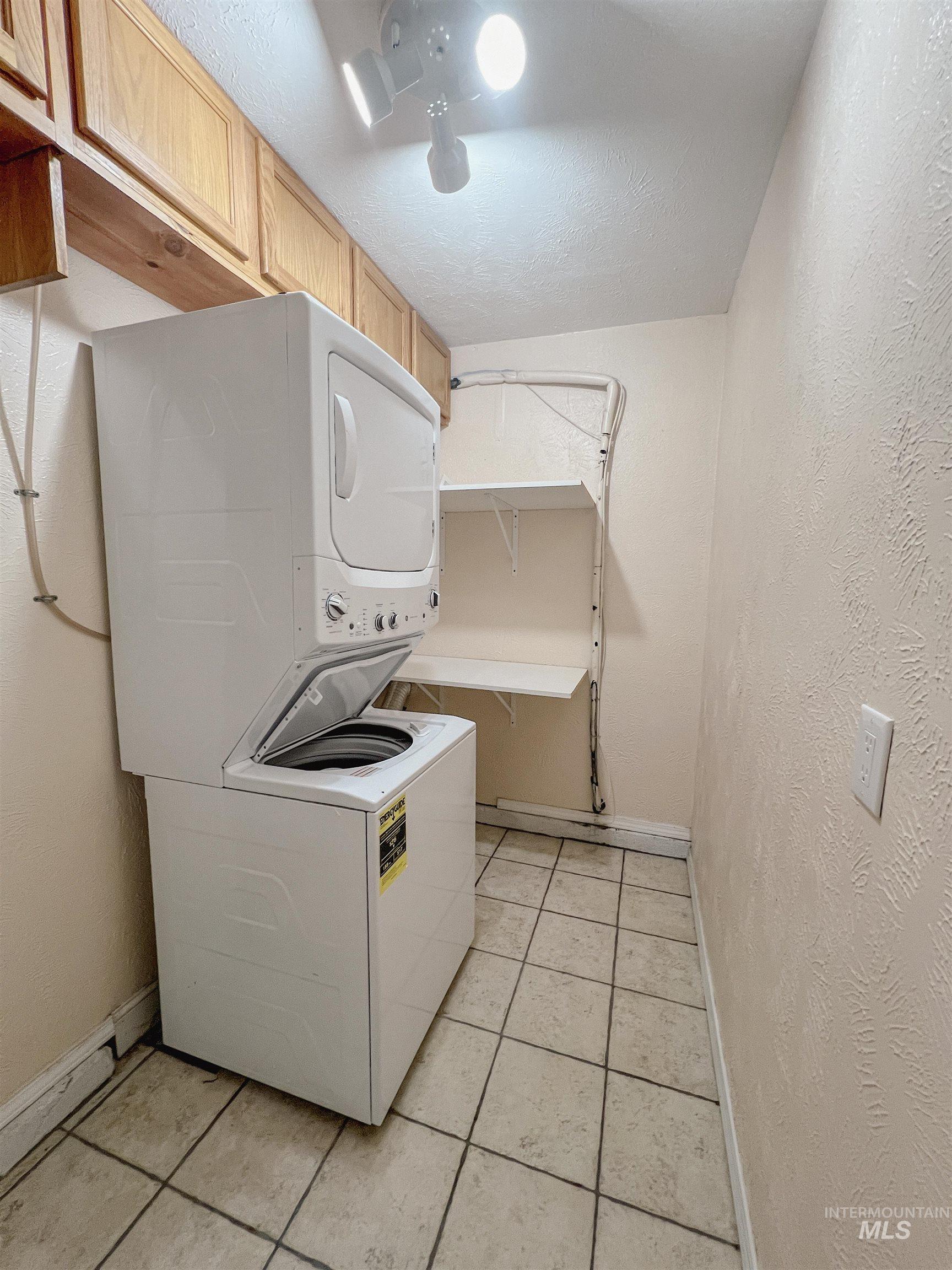 Laundry area with a textured wall, stacked washer and dryer, light tile patterned floors, and a textured ceiling