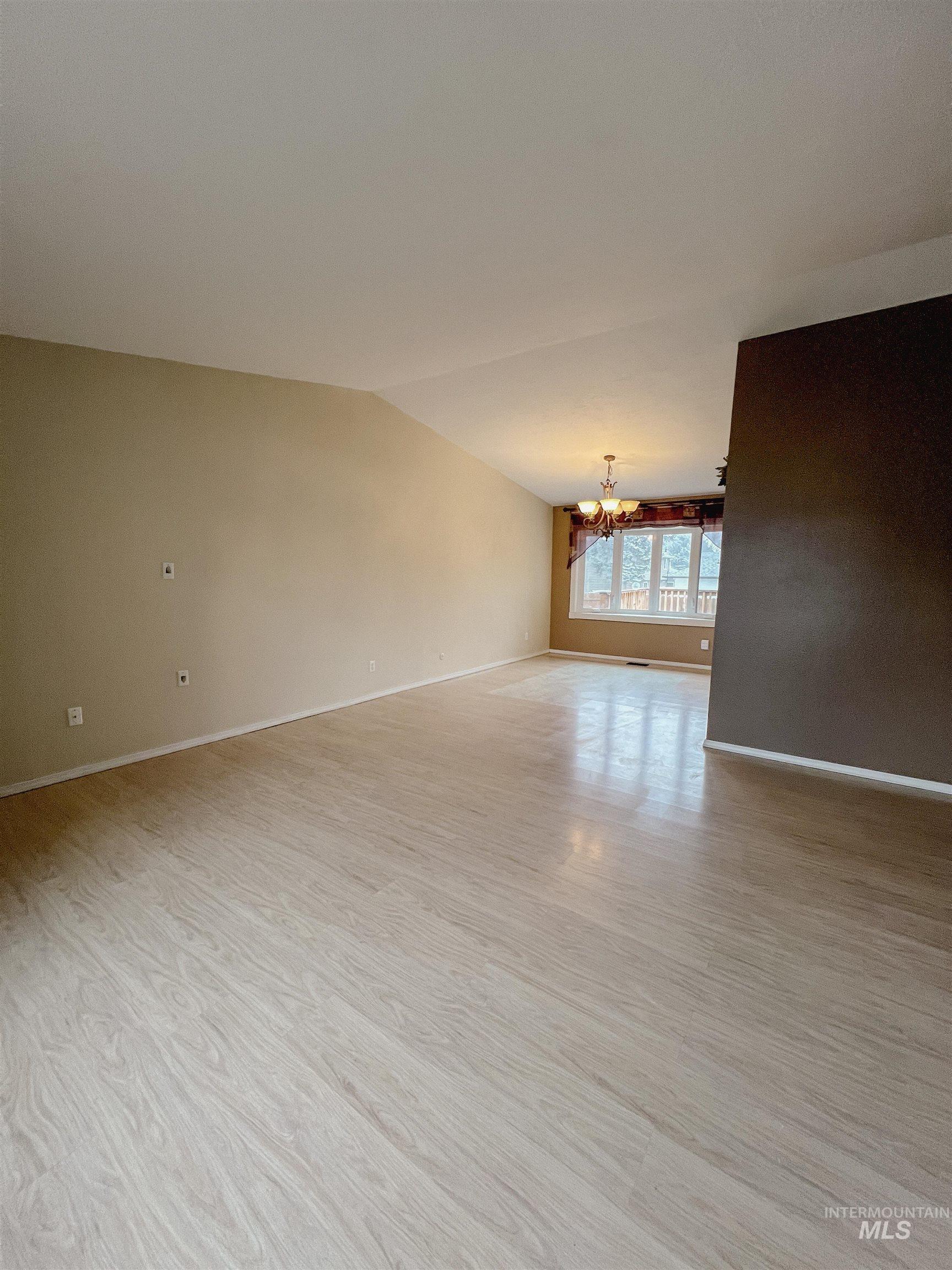 Unfurnished room featuring hanging lights, vaulted ceiling, and light wood-style flooring