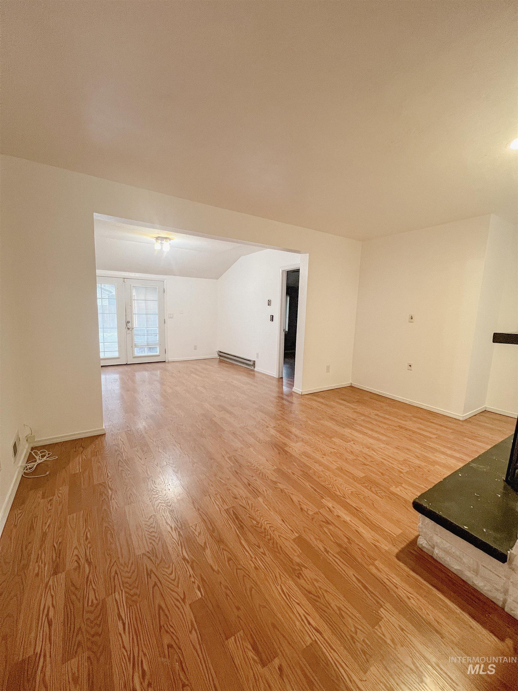 Unfurnished living room featuring light wood-style flooring, french doors, and baseboard heating